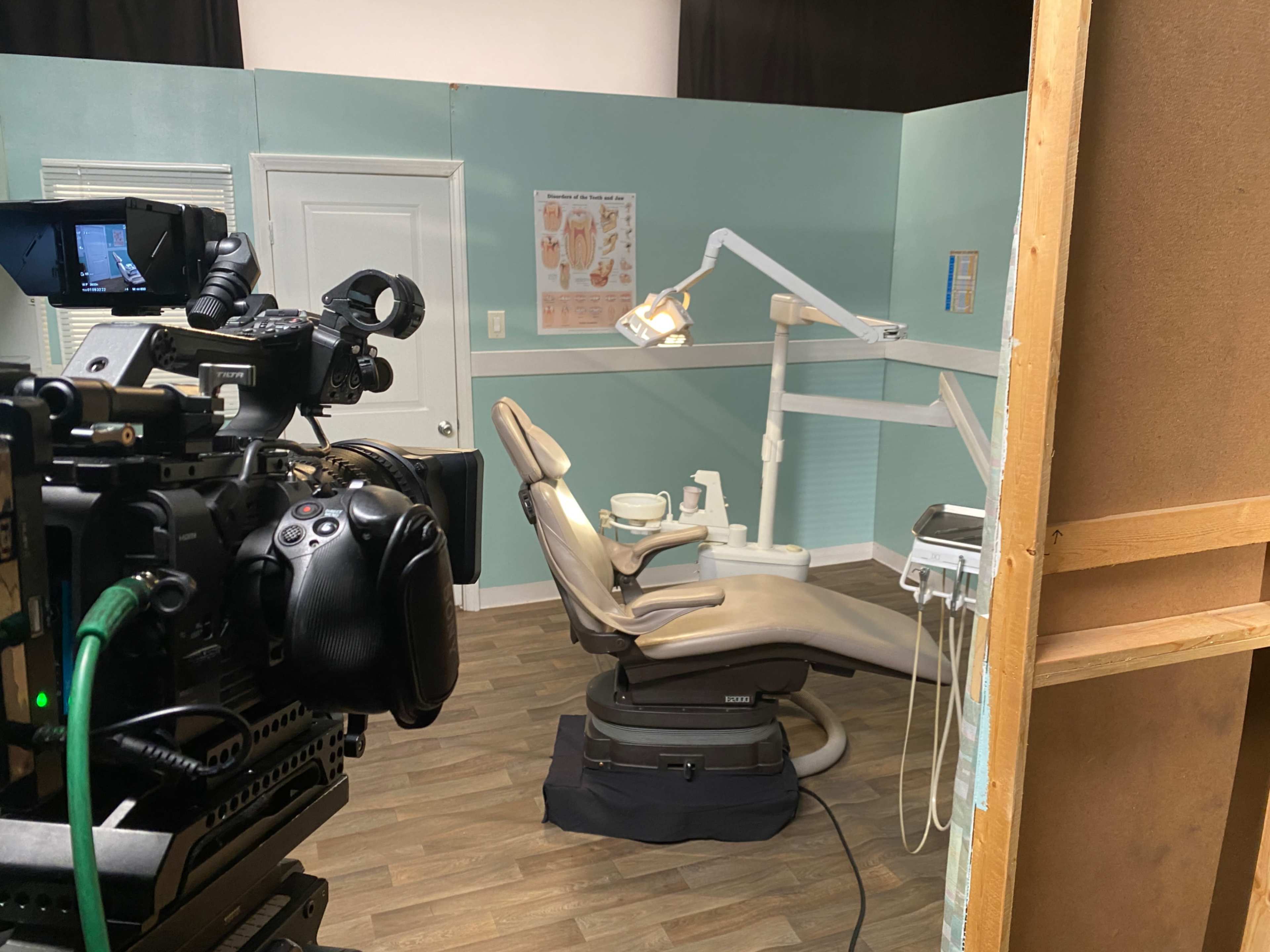 A dental office scene is shown with a dental chair, equipment, and a camera set up nearby.