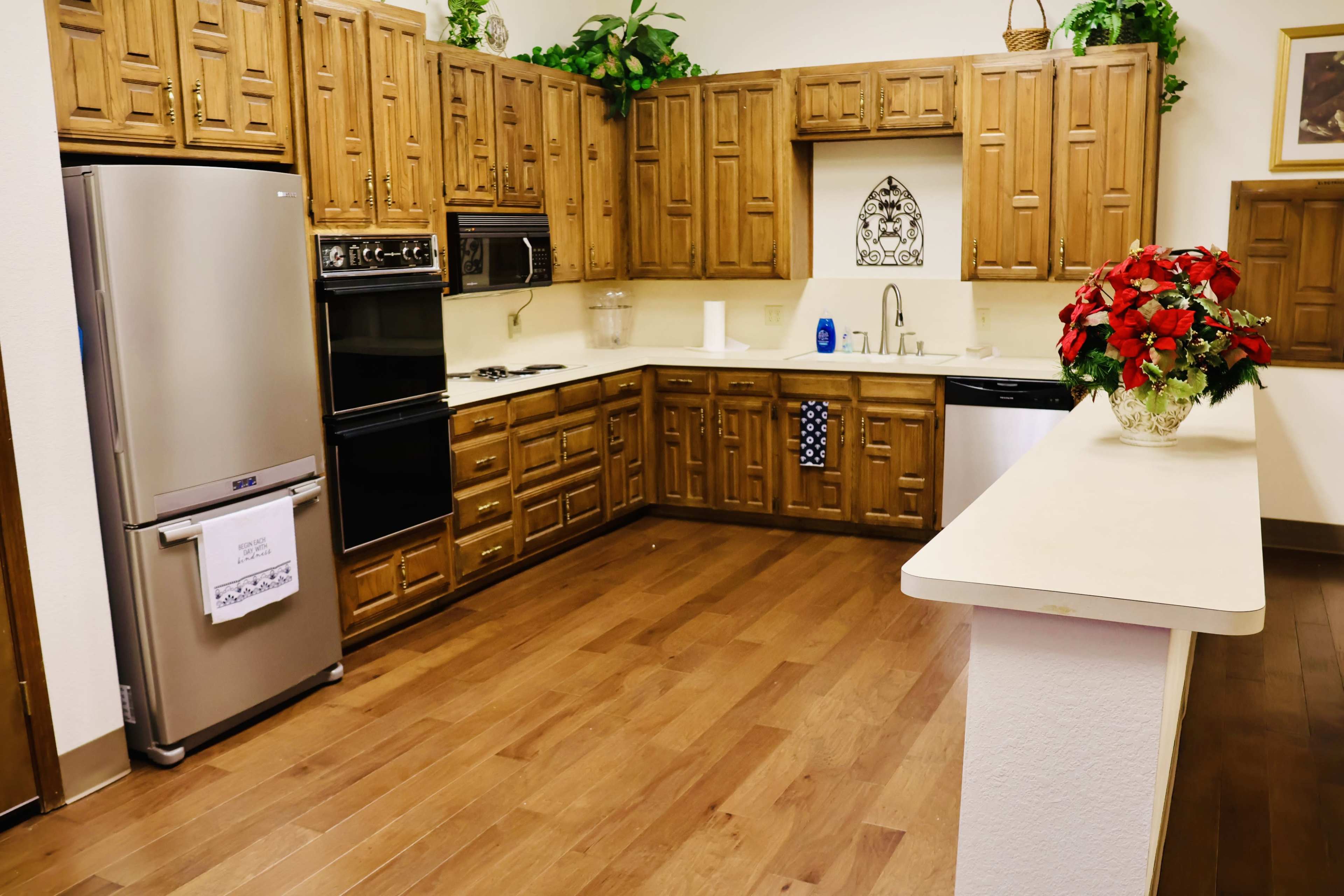 The image shows a kitchen with wooden cabinets, a stainless steel refrigerator, and a countertop separating it from a living area.