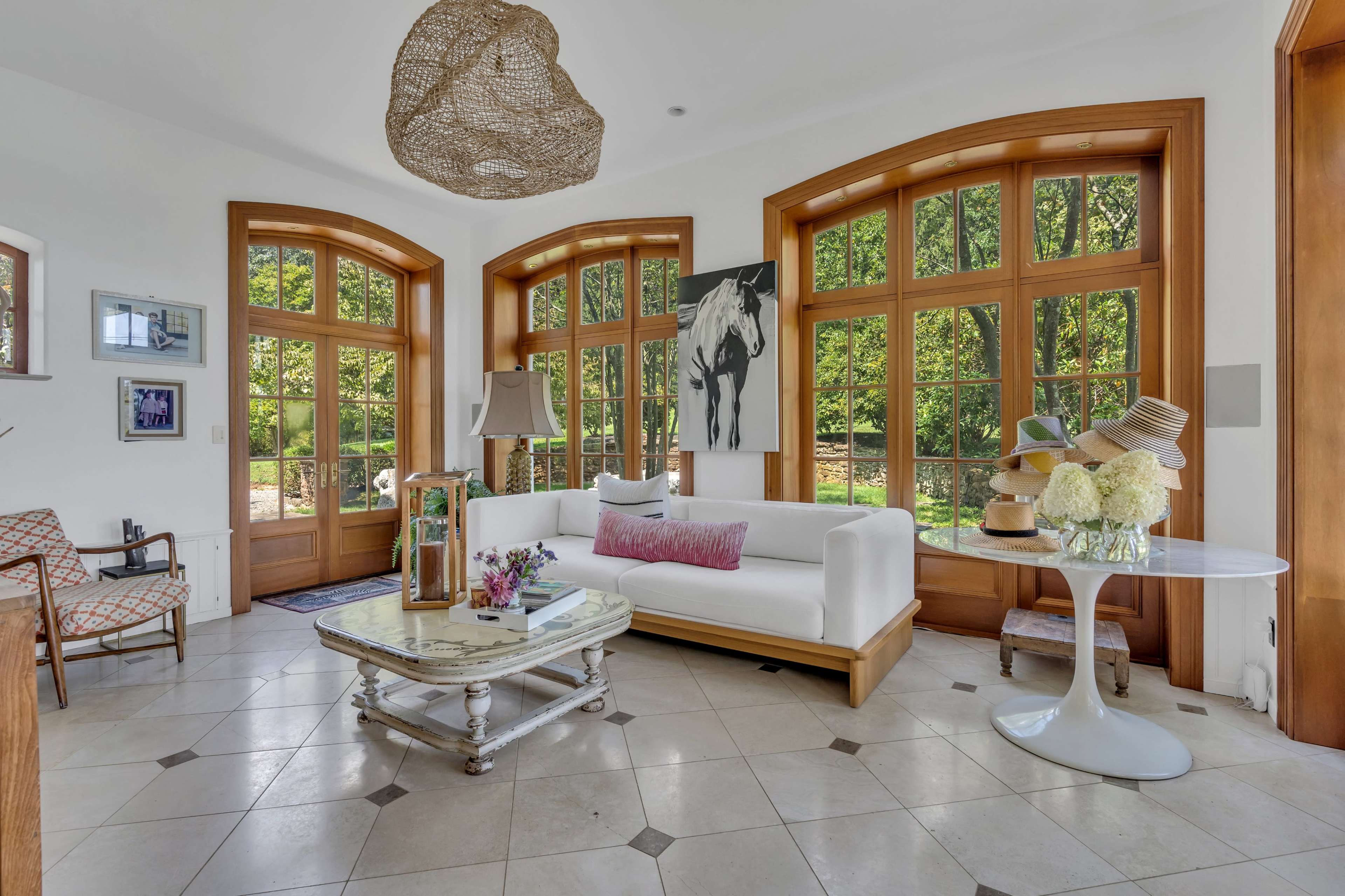The living room features large windows and a white sofa, with a round table and decorative elements arranged around a tiled floor.