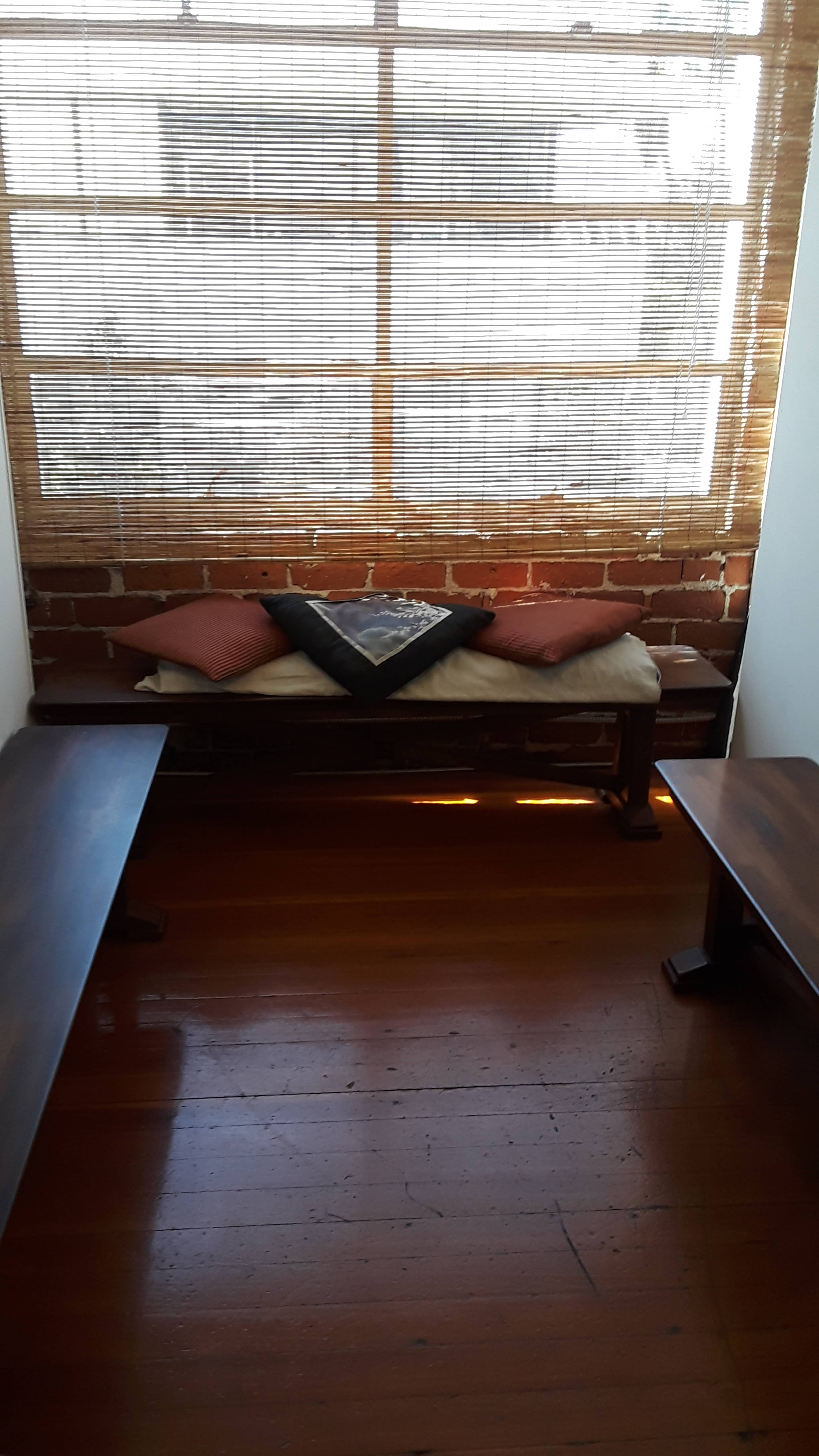 A small room with wooden benches on either side and a window with blinds allowing light to filter in, revealing a brick wall outside.