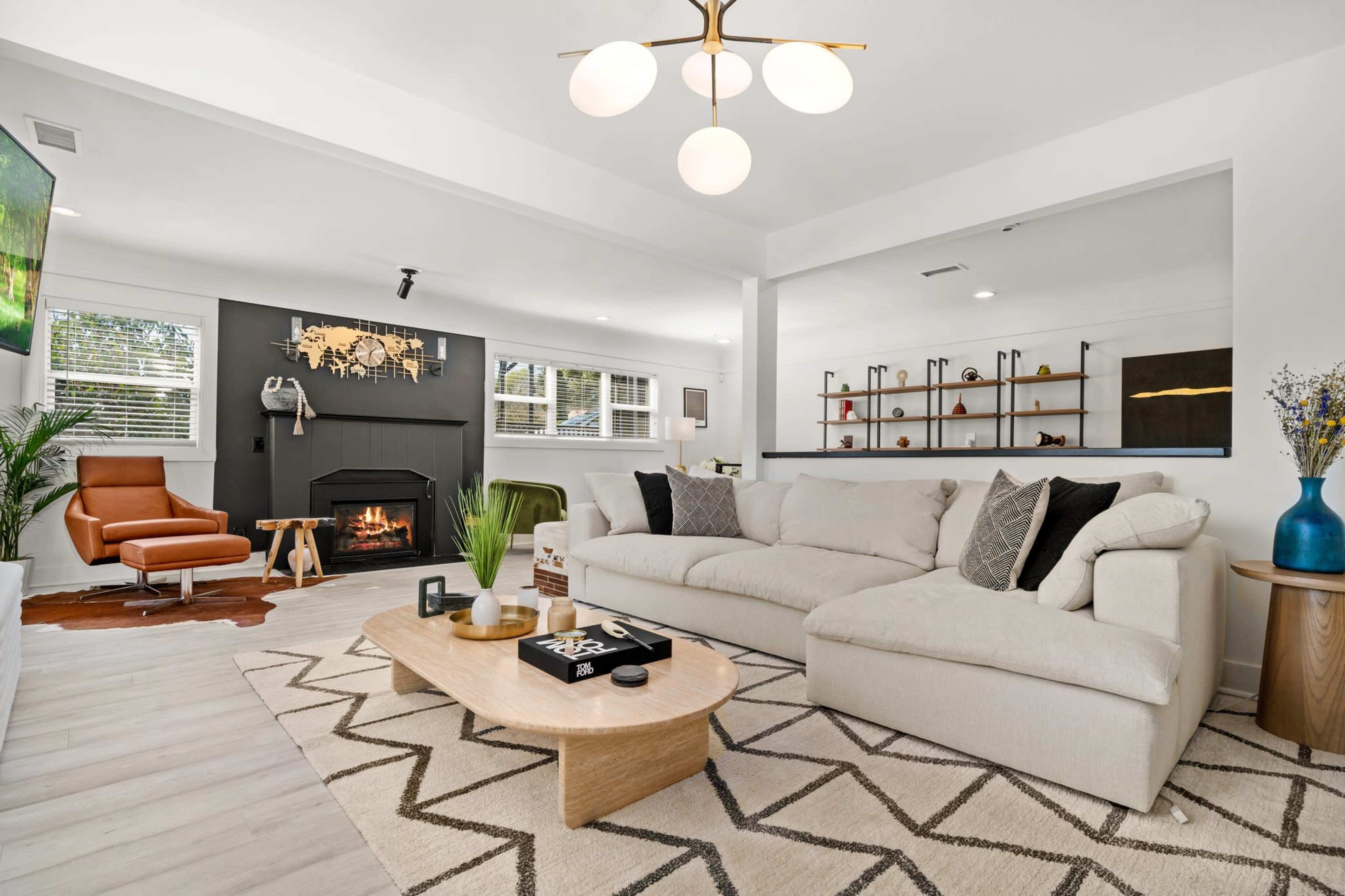 A modern living room with a beige sectional sofa, a wooden coffee table, a fireplace against a dark wall, and various decorative elements on shelves.