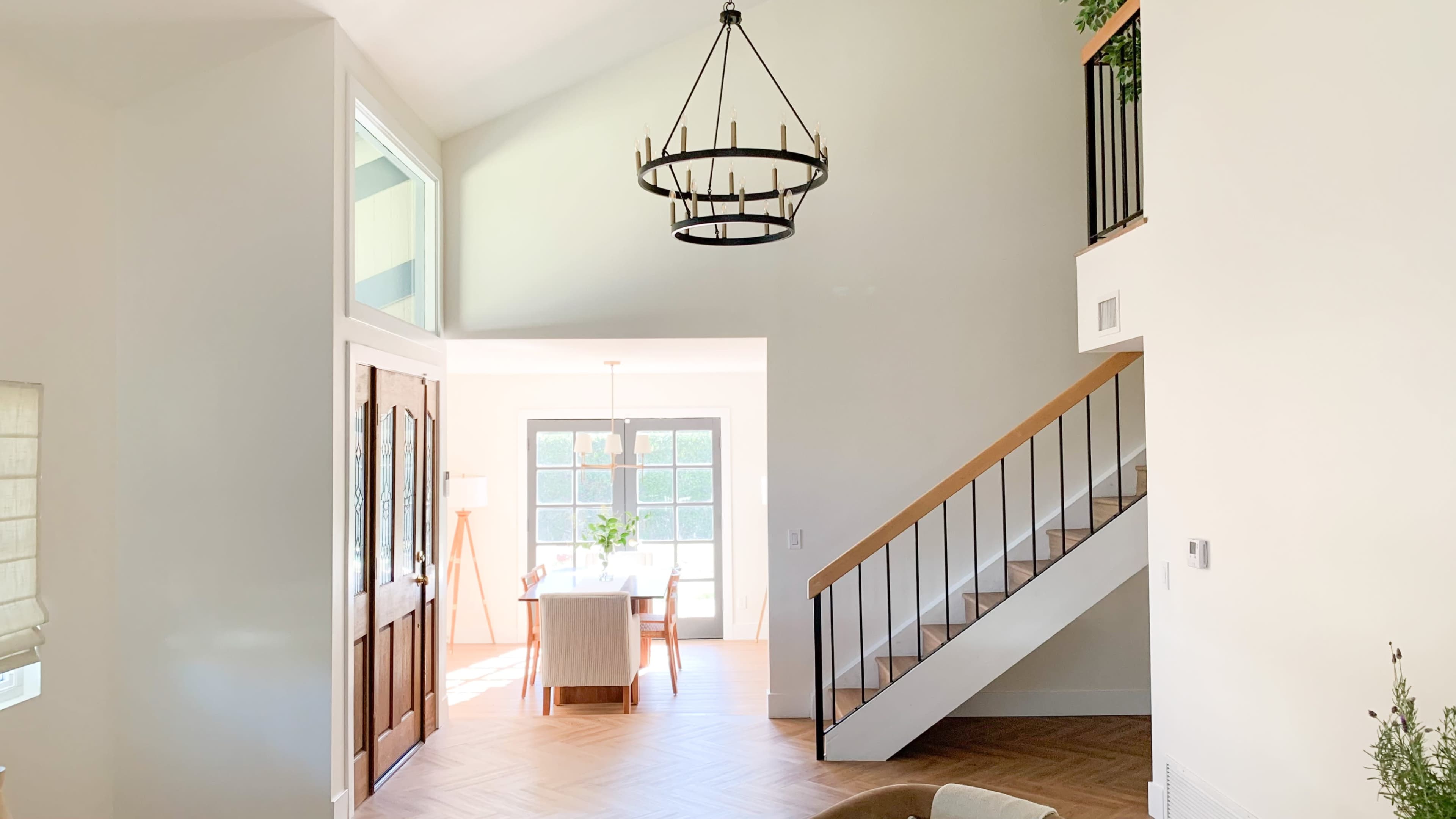 A bright, open interior space with a staircase on the right, a chandelier hanging from the ceiling, and a dining area visible through a doorway.