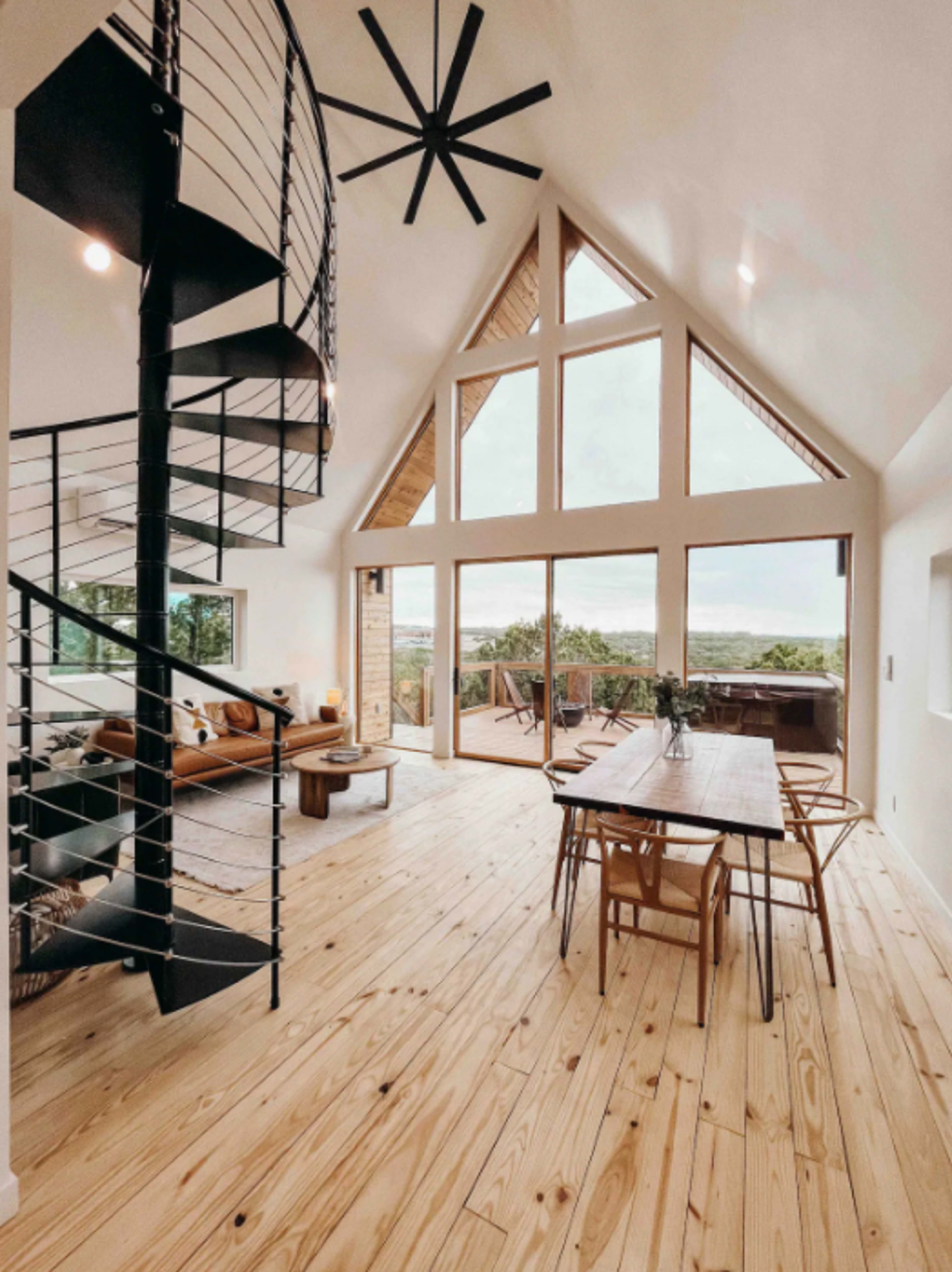 A modern interior with a spiral staircase, a large dining table, and floor-to-ceiling windows offering a view of the landscape.