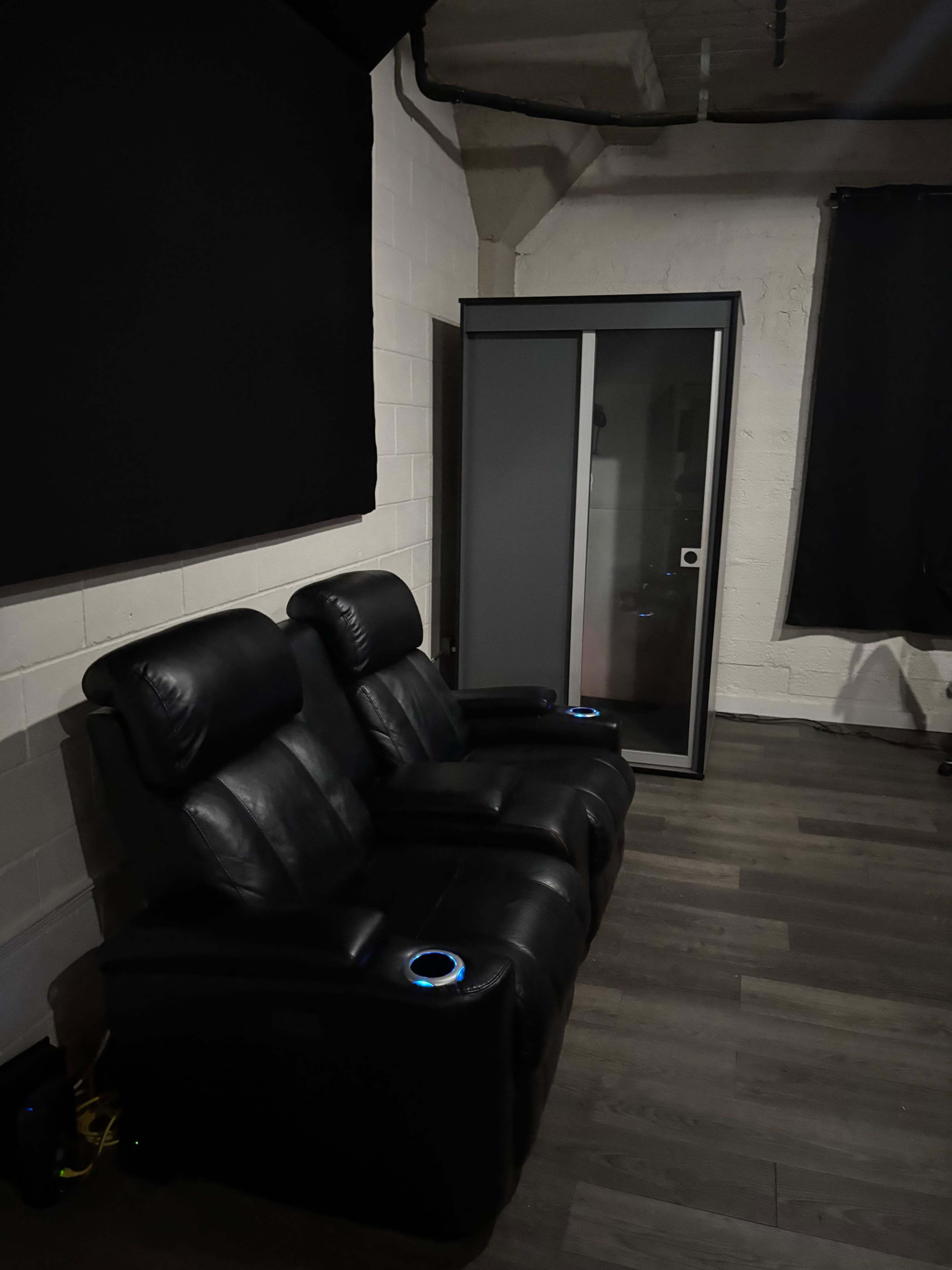 The image shows a seating area with two black leather recliners and a storage cabinet in a room with a neutral color scheme.