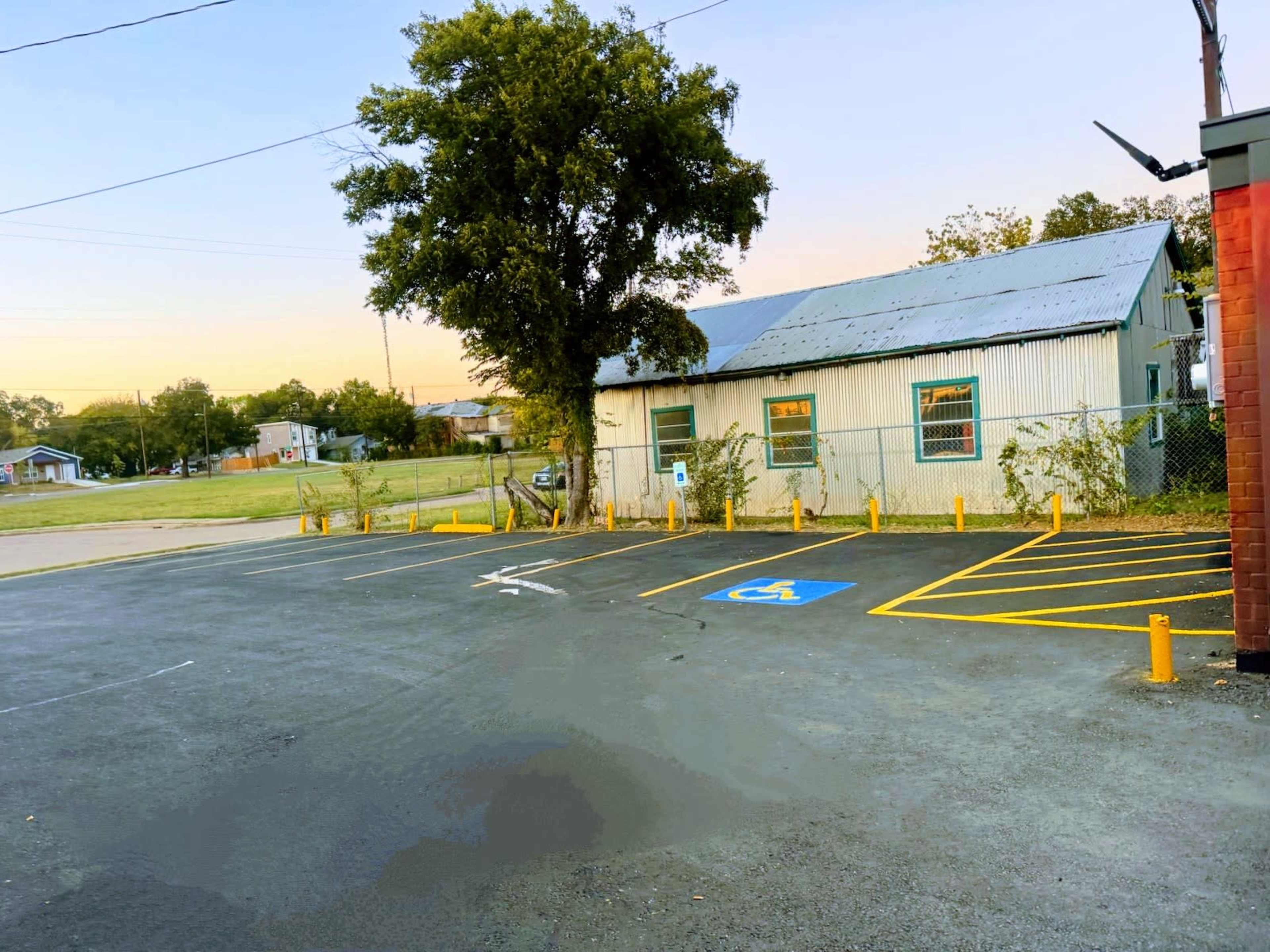 The image shows a parking lot with marked spaces, including a handicapped space, next to a metal building with a corrugated roof and trees in the background.