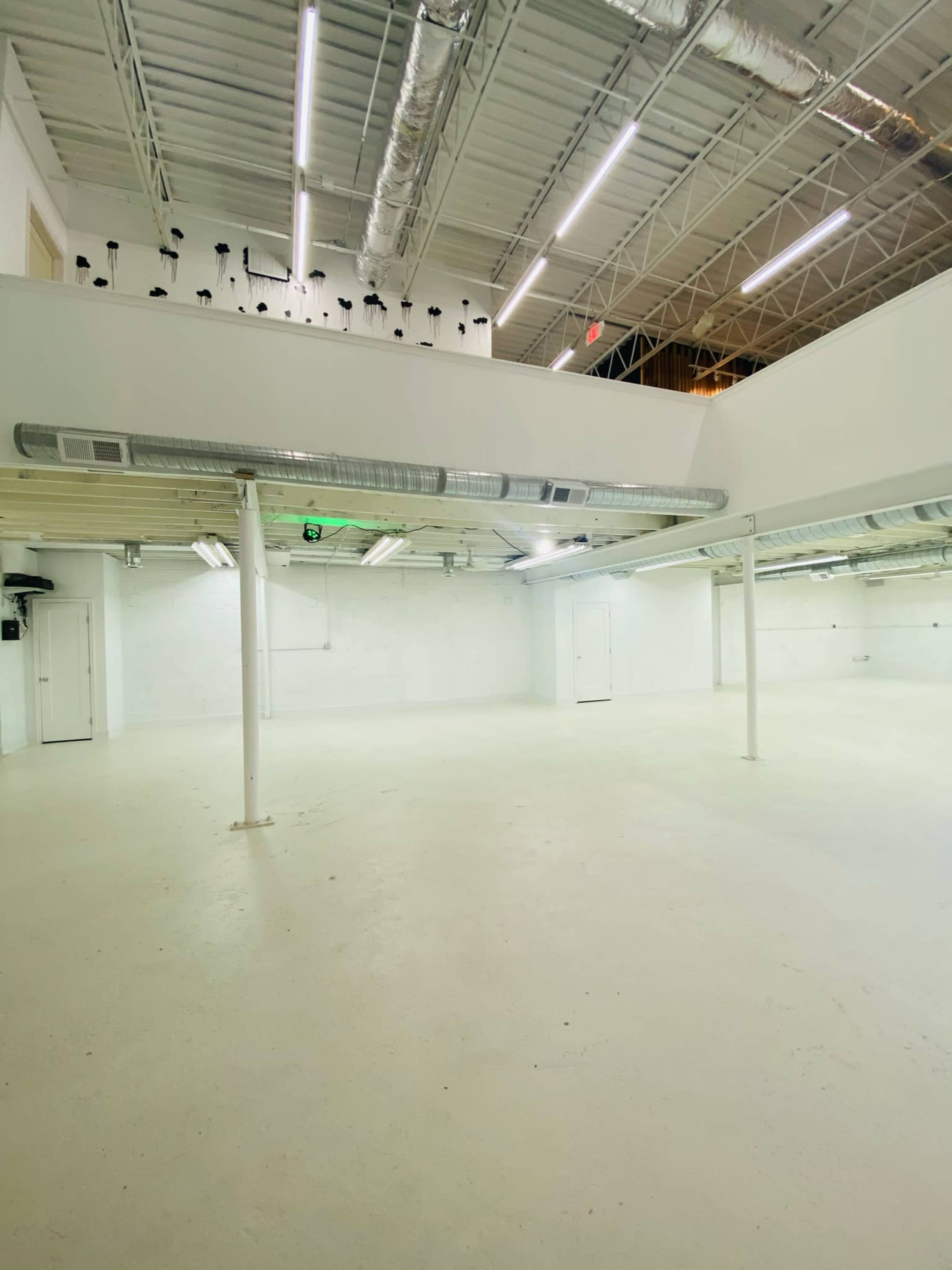 A spacious, empty interior of a building with white walls, a high ceiling, and exposed ductwork.