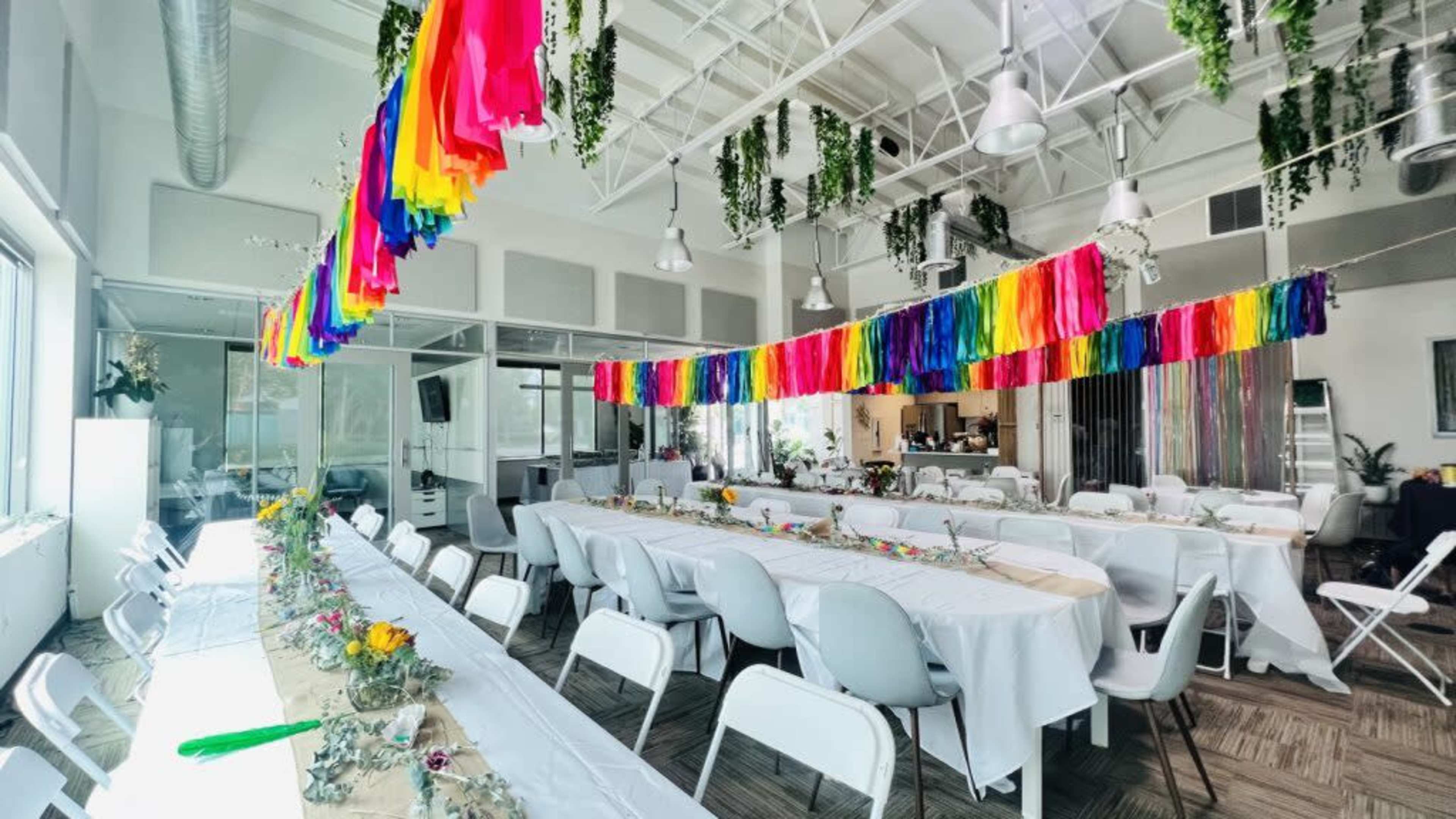 A brightly decorated event space features long tables set with flowers and colorful streamers hanging from the ceiling.