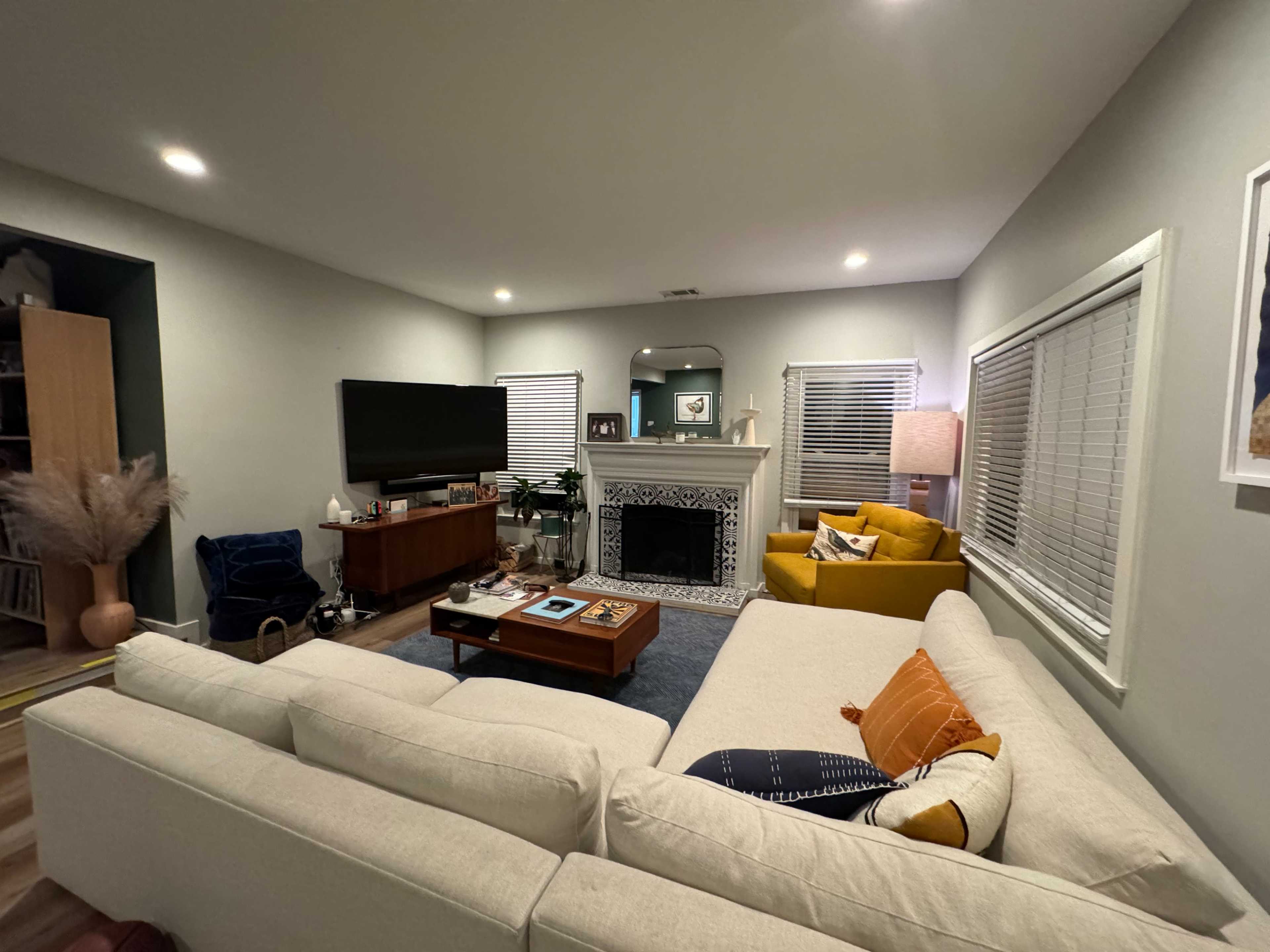 The living room features a large sectional sofa, a wooden coffee table, a television set, and a decorative fireplace, with a mix of modern and cozy furnishings.