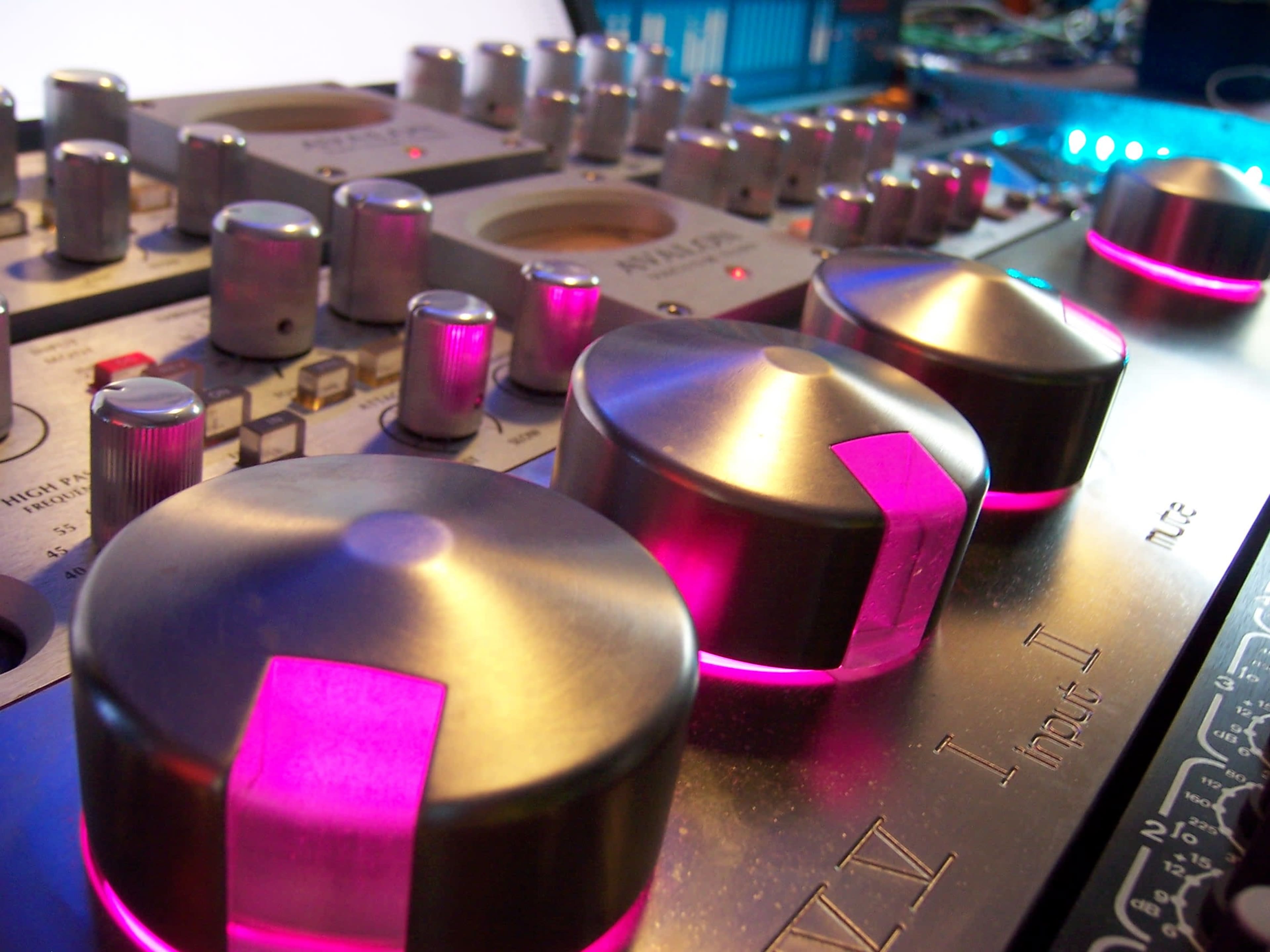 A close-up of a music mixer with metallic knobs and illuminated pink accents.