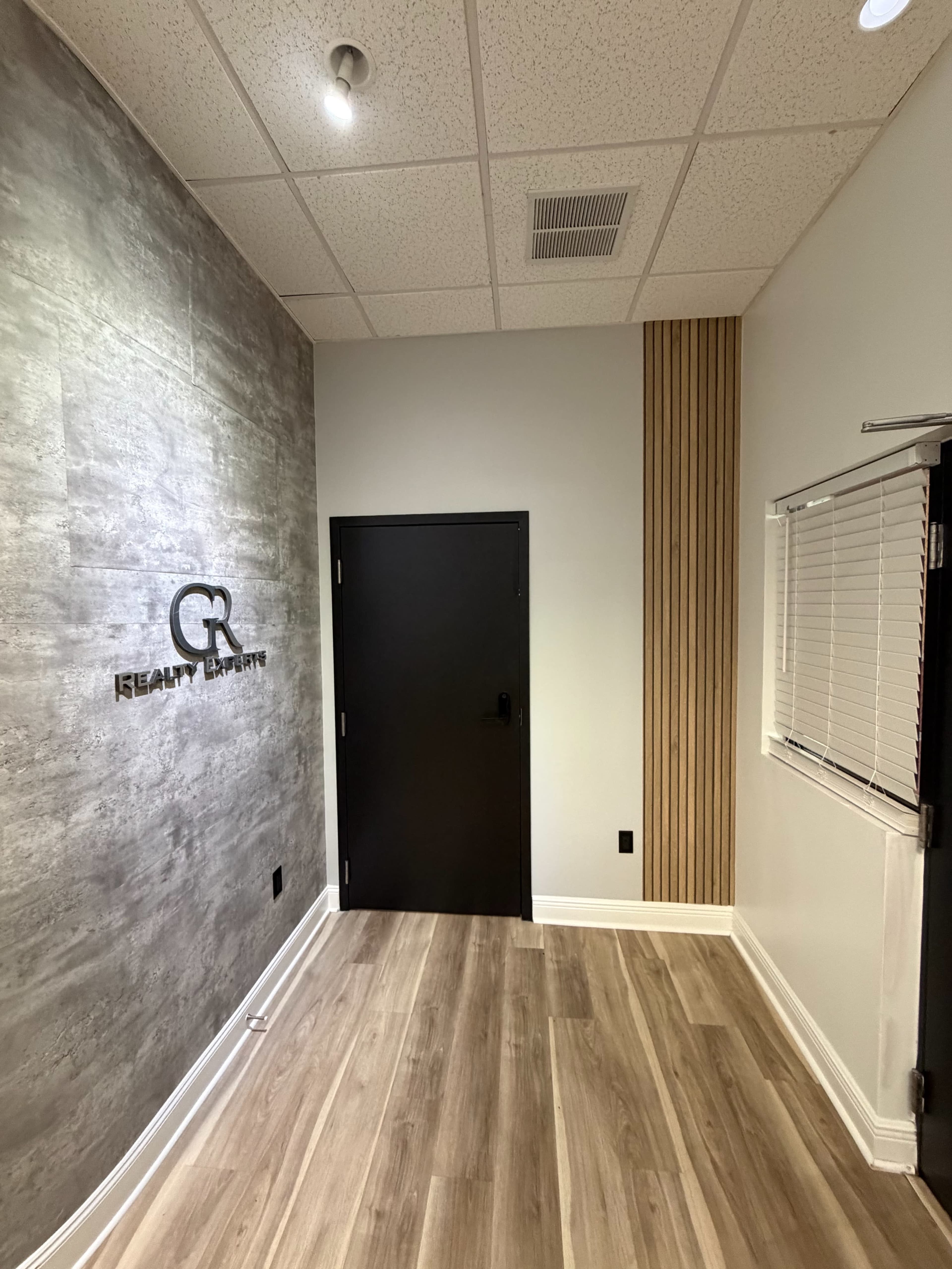 The image shows a modern interior space featuring textured gray walls, a black door, and wooden accent paneling.