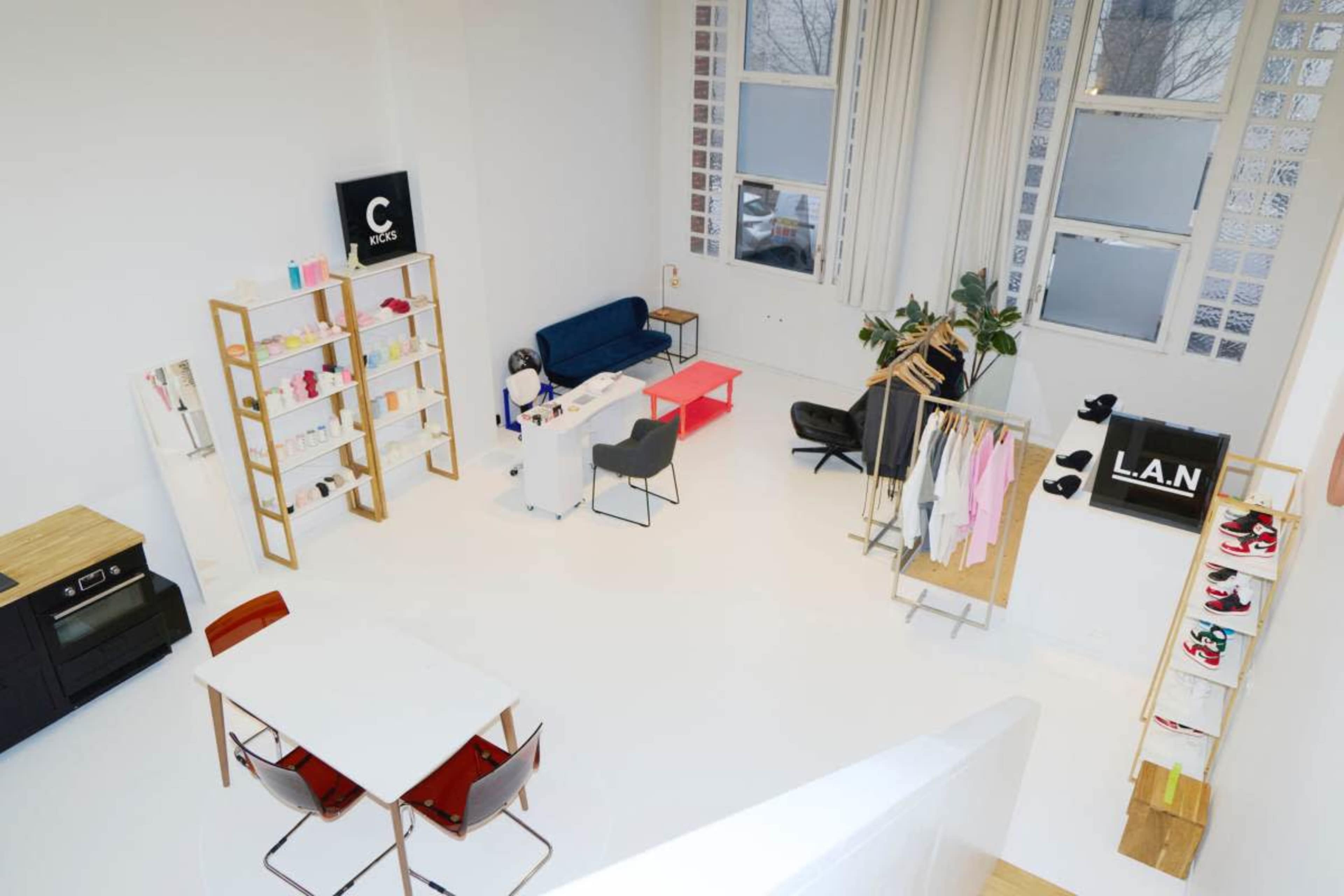 The image shows a modern retail space with minimal furniture, including shelving, a seating area, and a display of clothing and shoes.