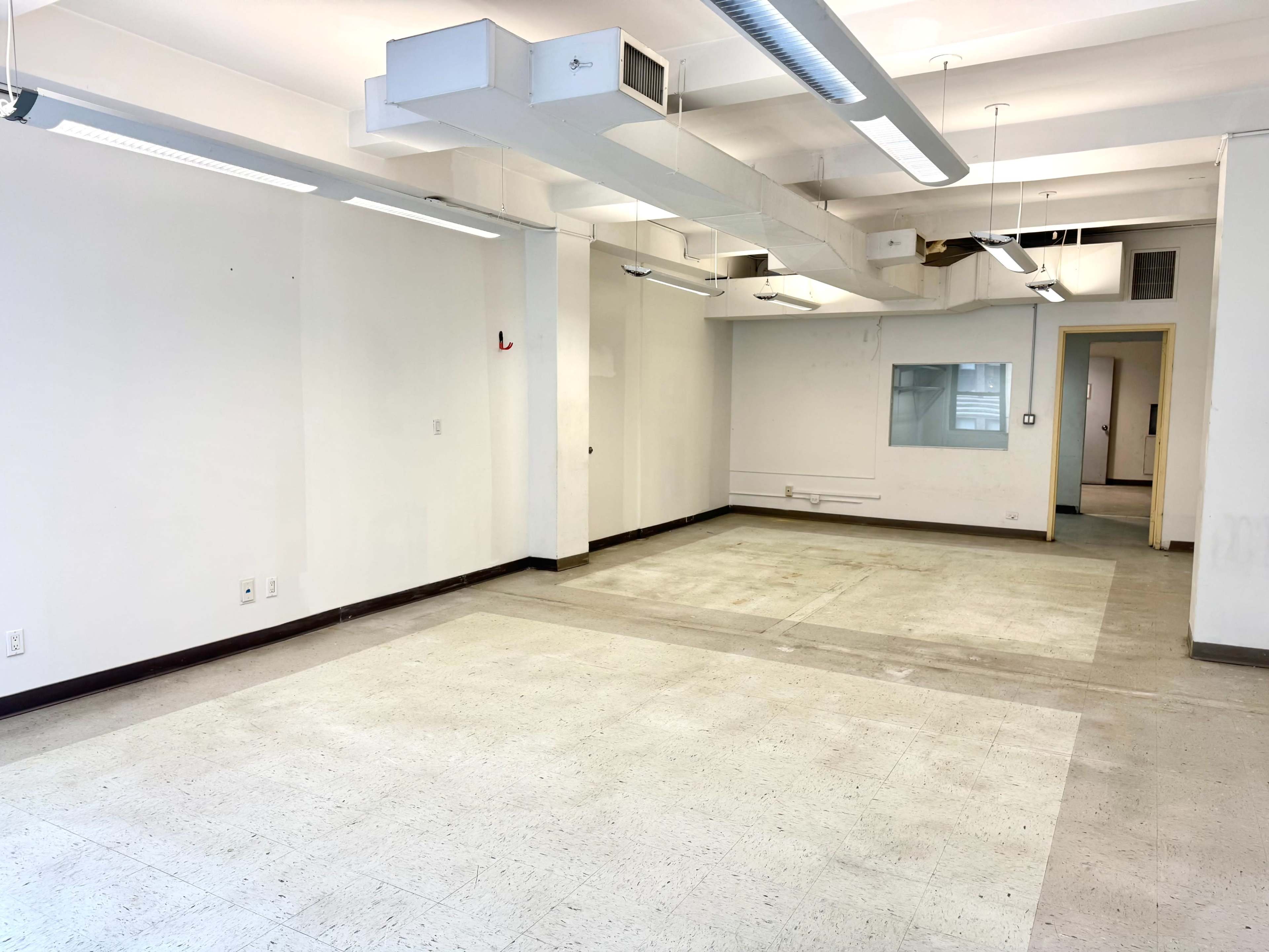 The image shows an empty room with concrete flooring, white walls, and overhead lighting.