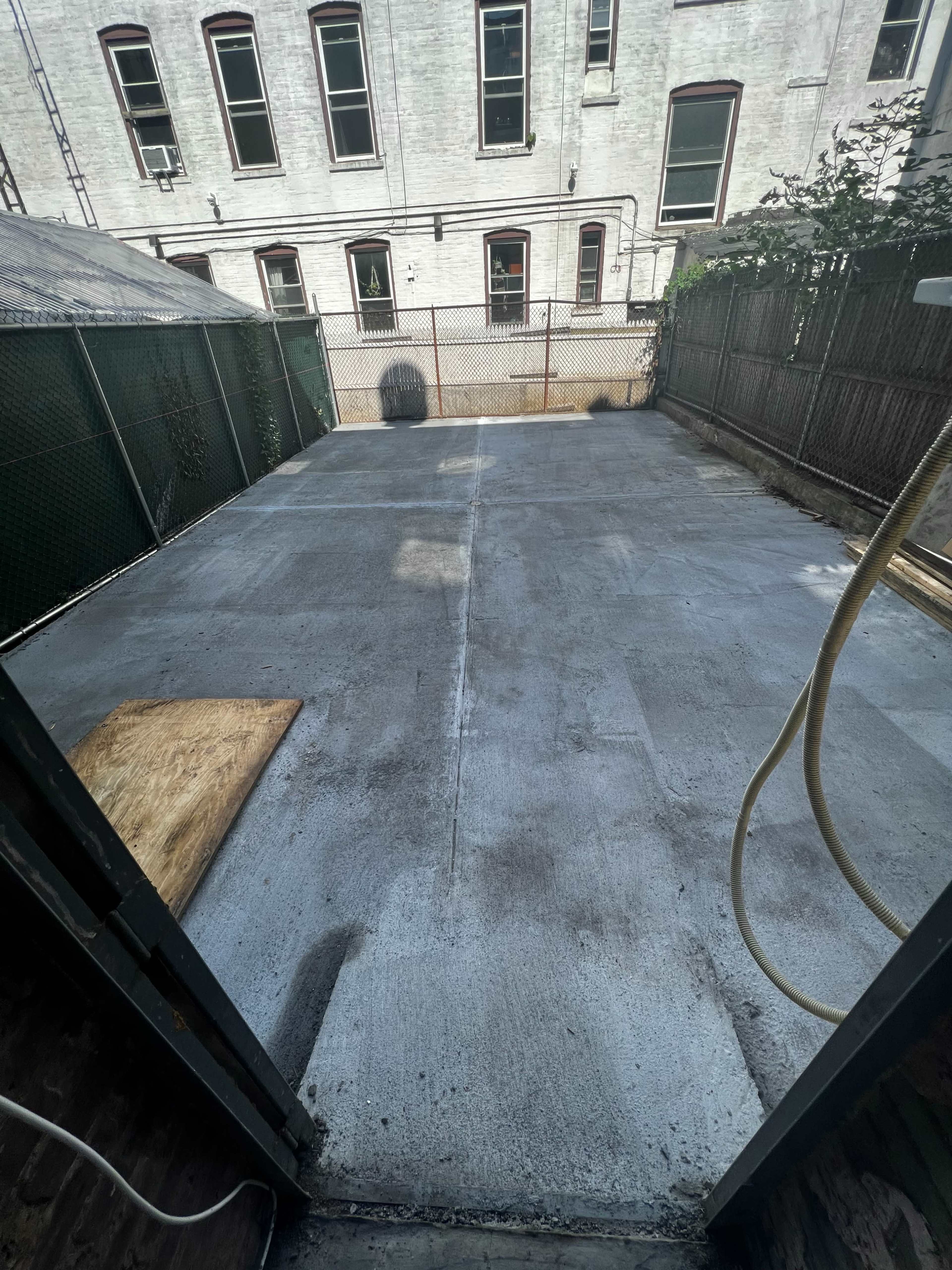 The image shows a vacant concrete patio area enclosed by a fence and surrounded by buildings.
