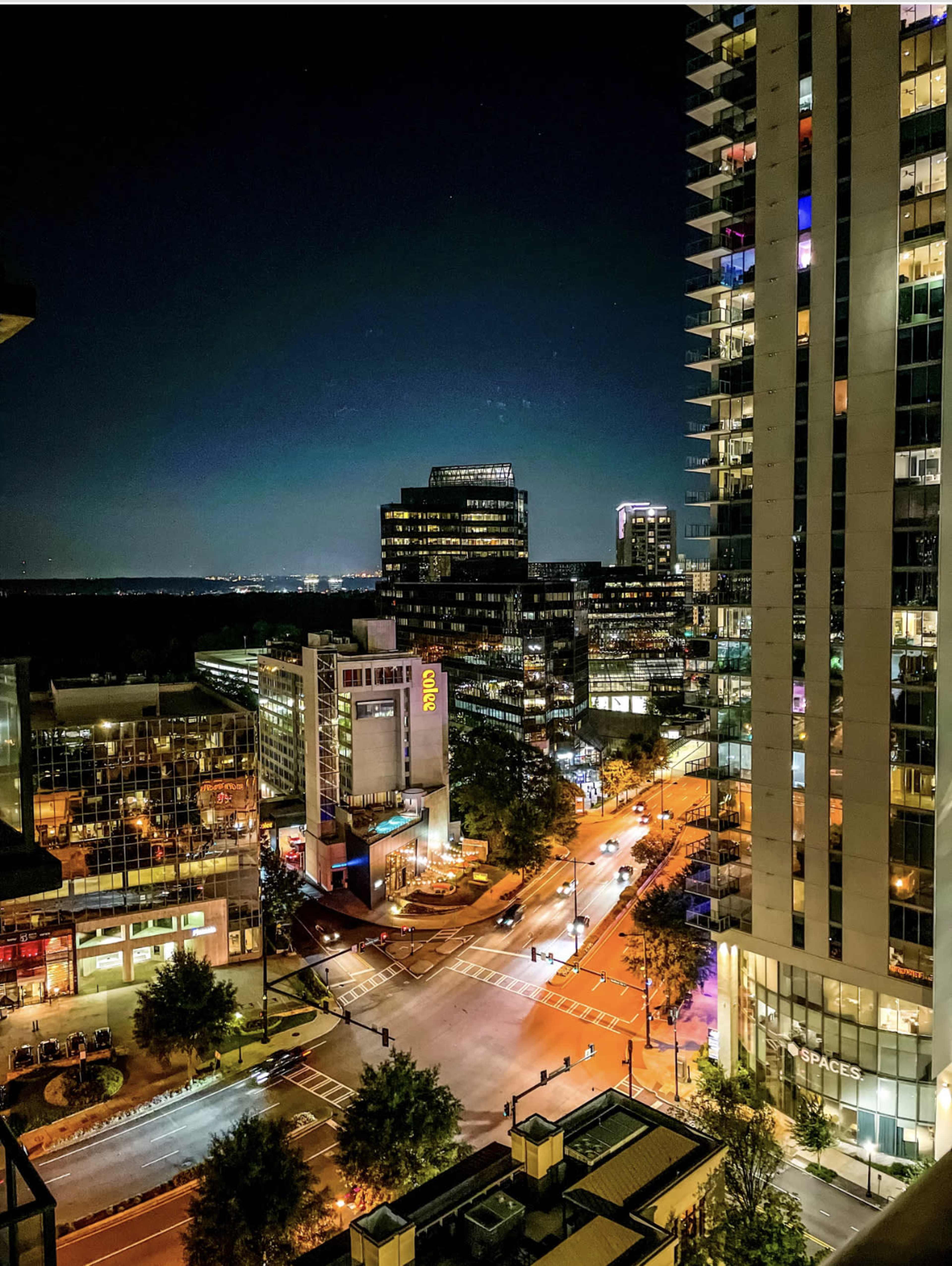 A city skyline at night, featuring illuminated buildings and busy streets.