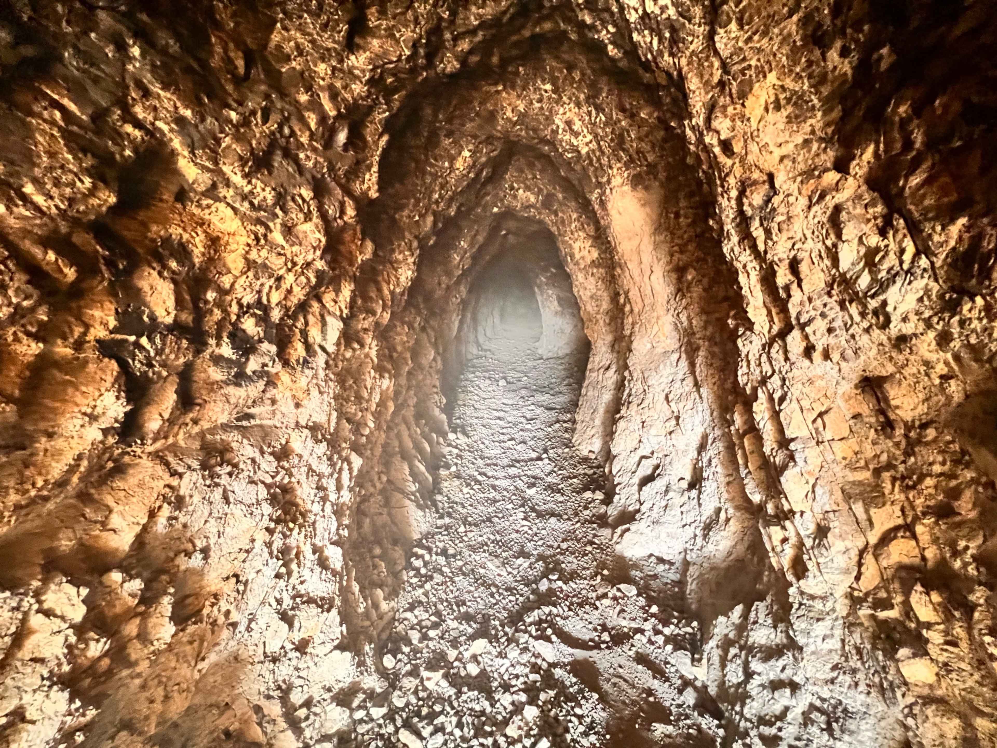 A narrow, dimly lit tunnel with rocky walls and a gravel floor.
