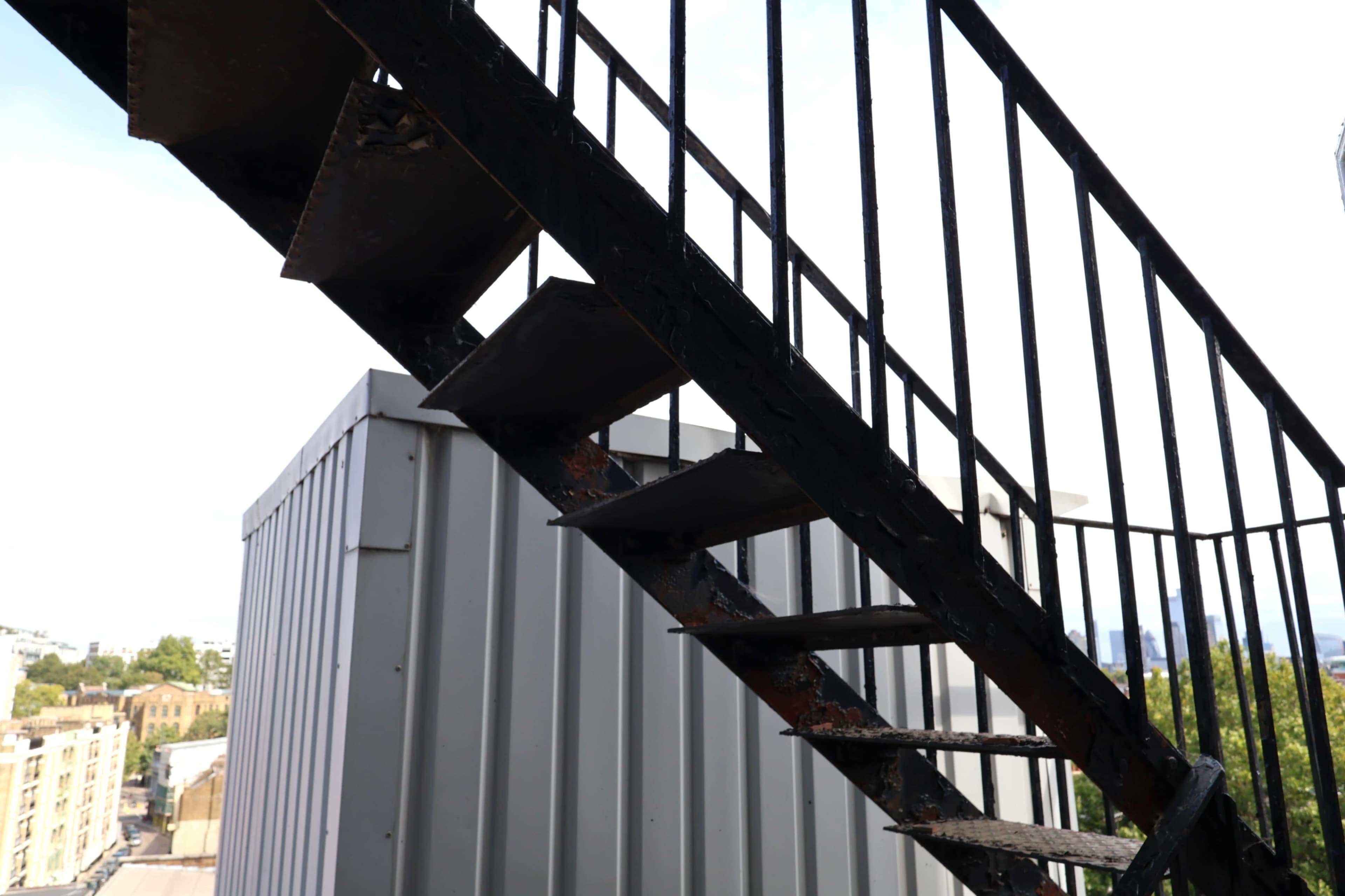 A metal staircase ascends against a gray rooftop structure under a bright sky.