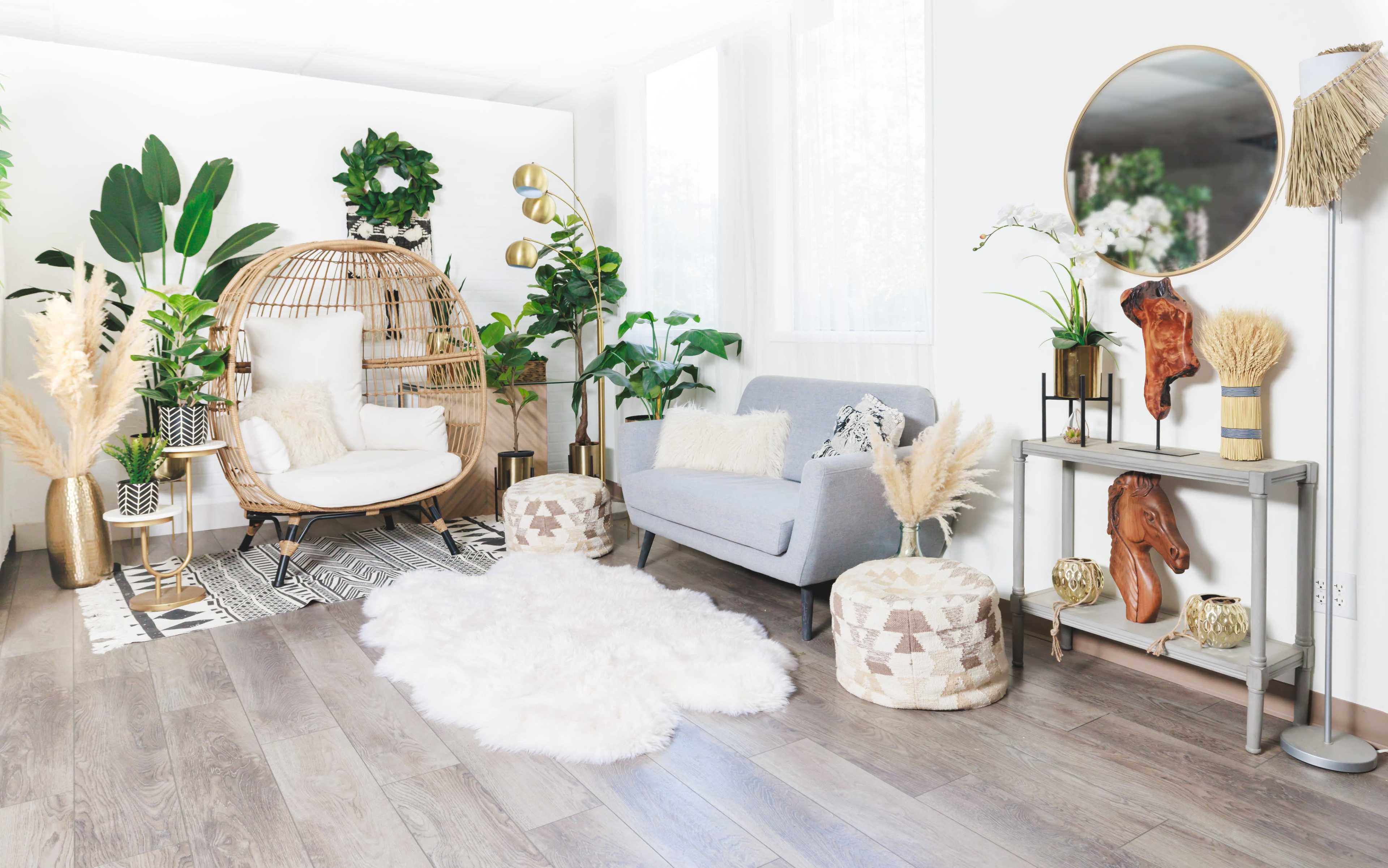 A modern living room with plants, a rattan chair, a gray sofa, decorative items, and a circular mirror against a light-colored wall.