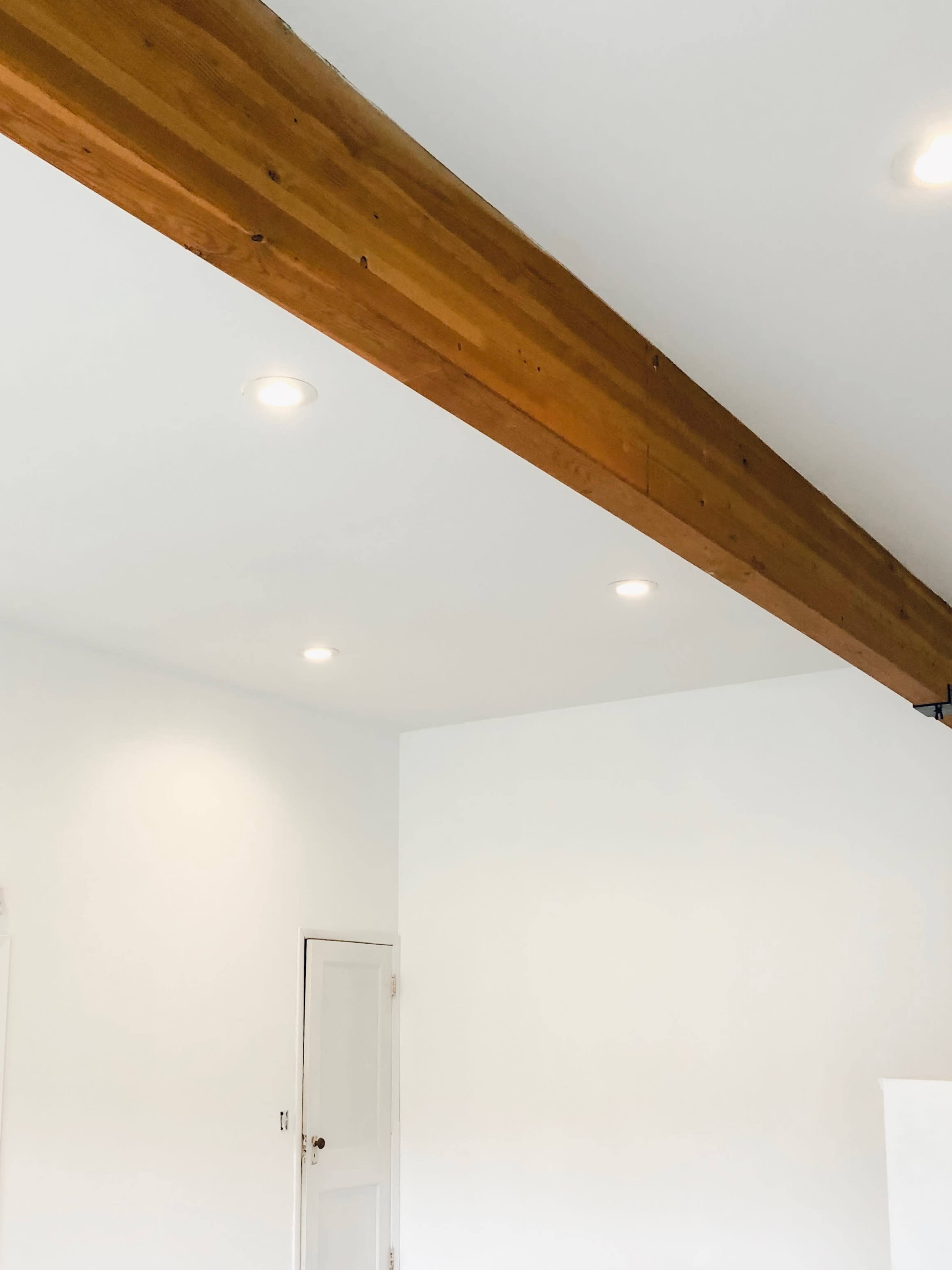A room with a wooden beam across the ceiling and recessed lights illuminating the walls.