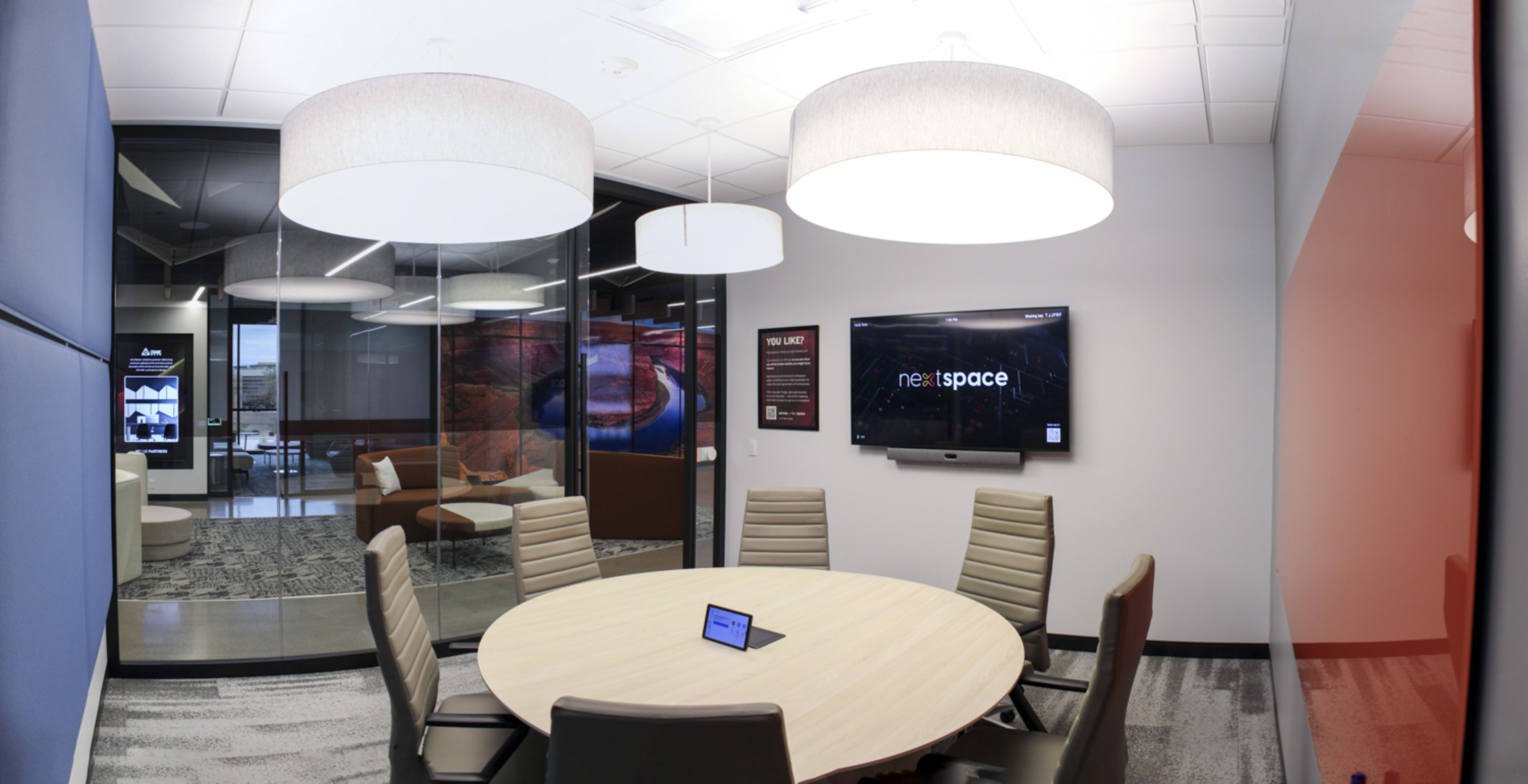 A conference room features a round table, modern seating, and large hanging light fixtures, with a screen displaying "nextspace" on one wall.