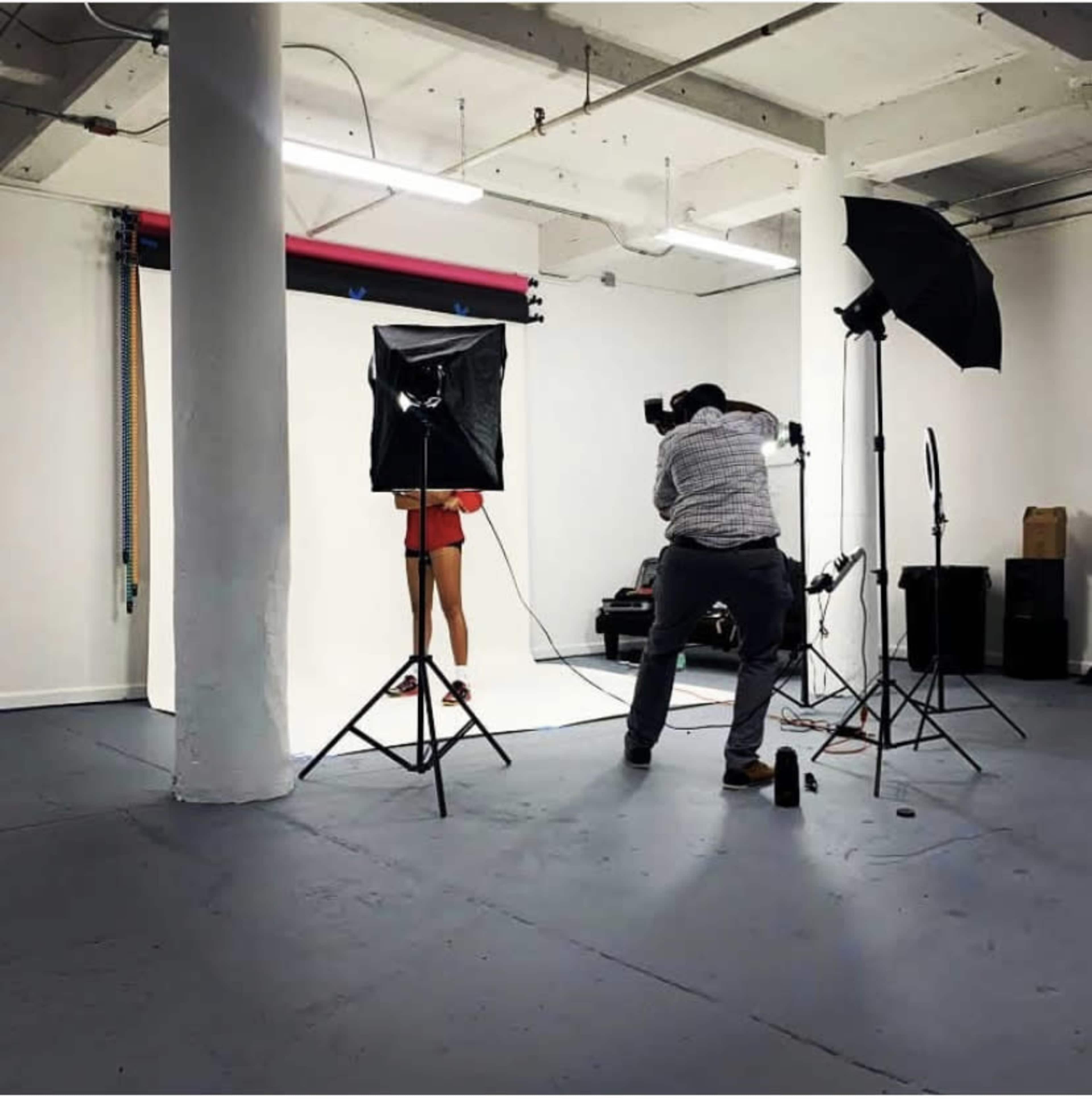 A photographer is capturing images in a studio with a backdrop and several lighting equipment setup.