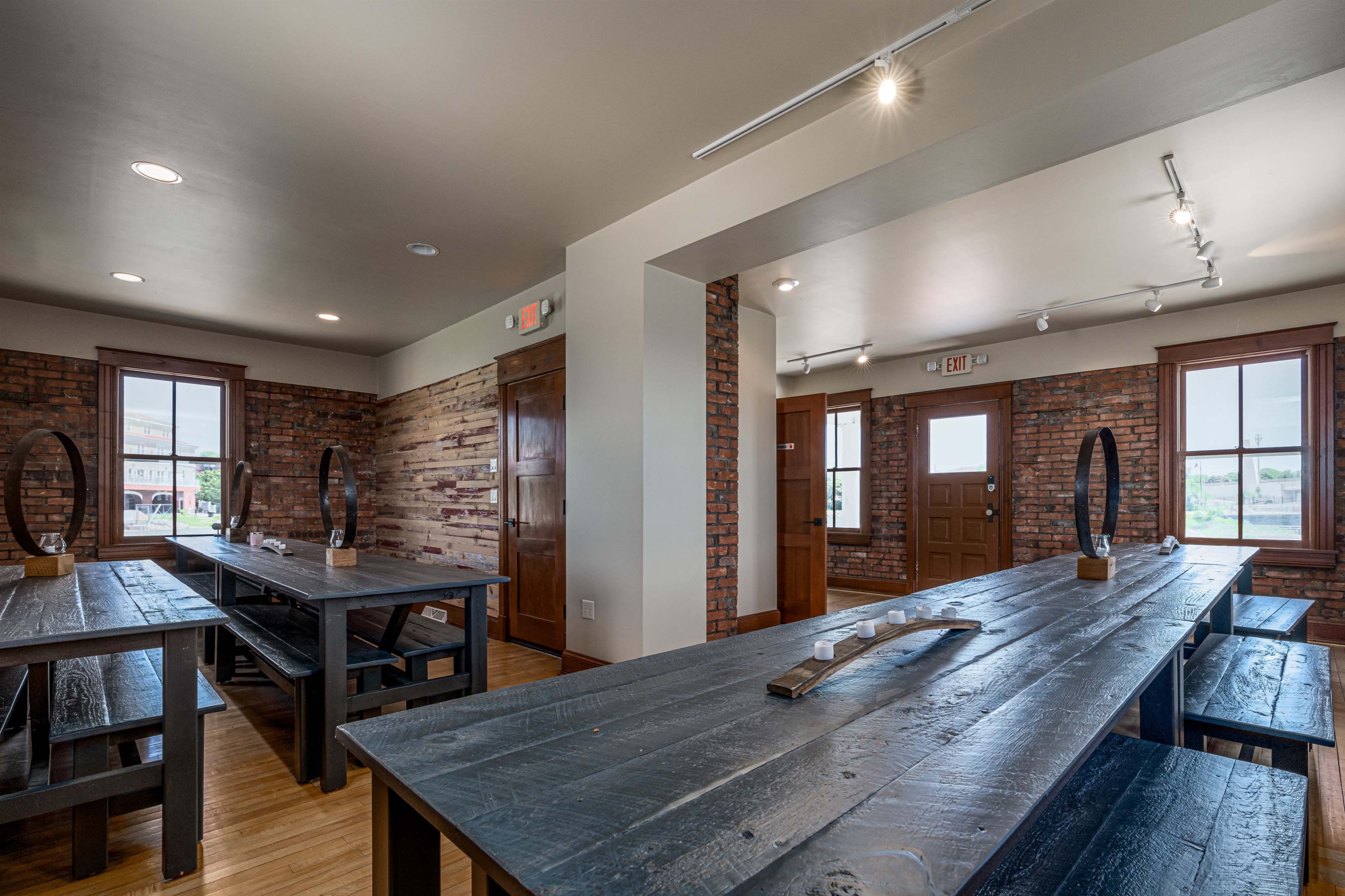 A modern dining area with wooden tables and benches, exposed brick walls, and large windows letting in natural light.
