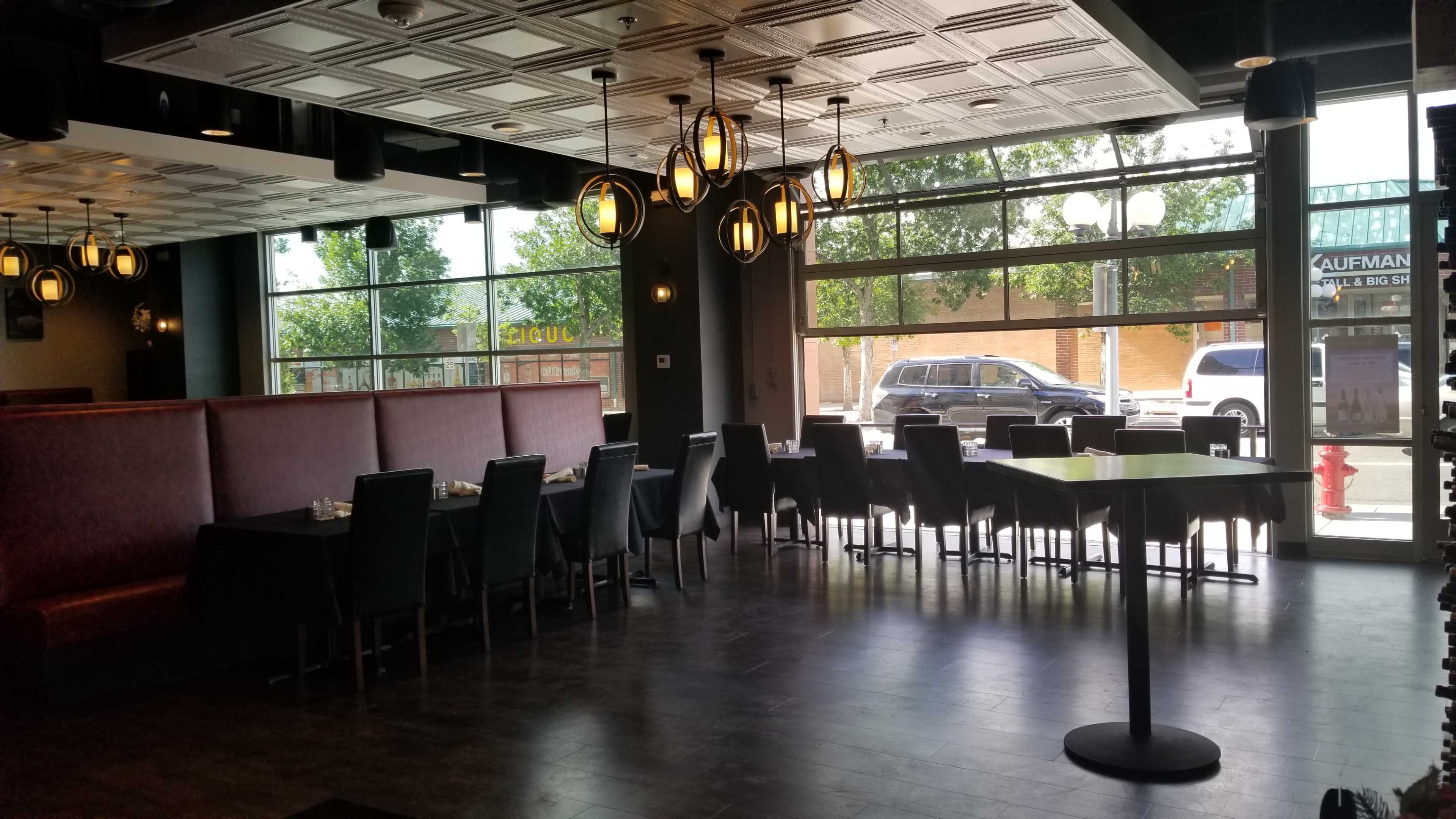 The image shows a spacious restaurant interior with dark furniture, large windows allowing natural light, and a mix of booth and table seating.
