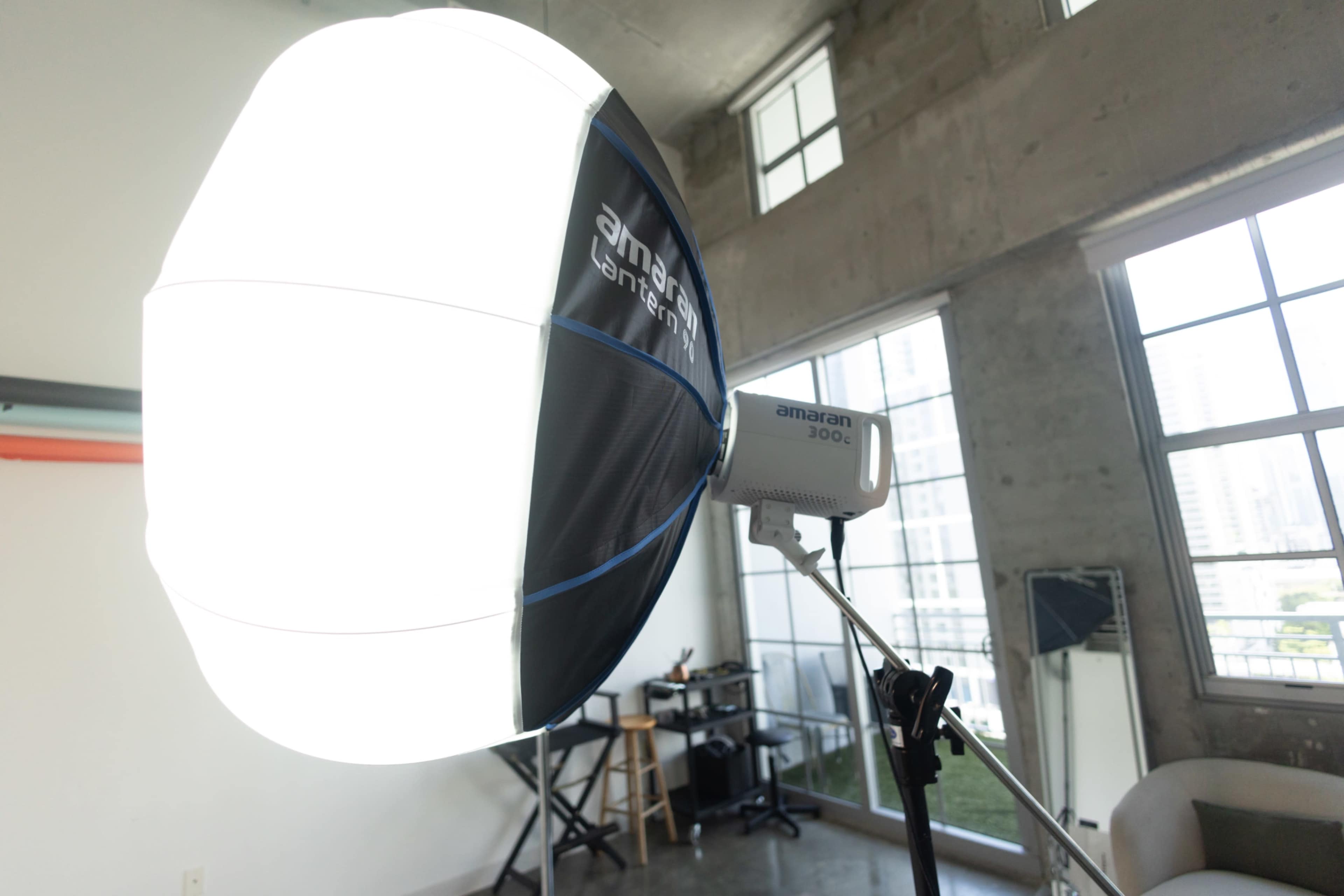 A large softbox is set up in a room with concrete walls and large windows, attached to a light source on a tripod.