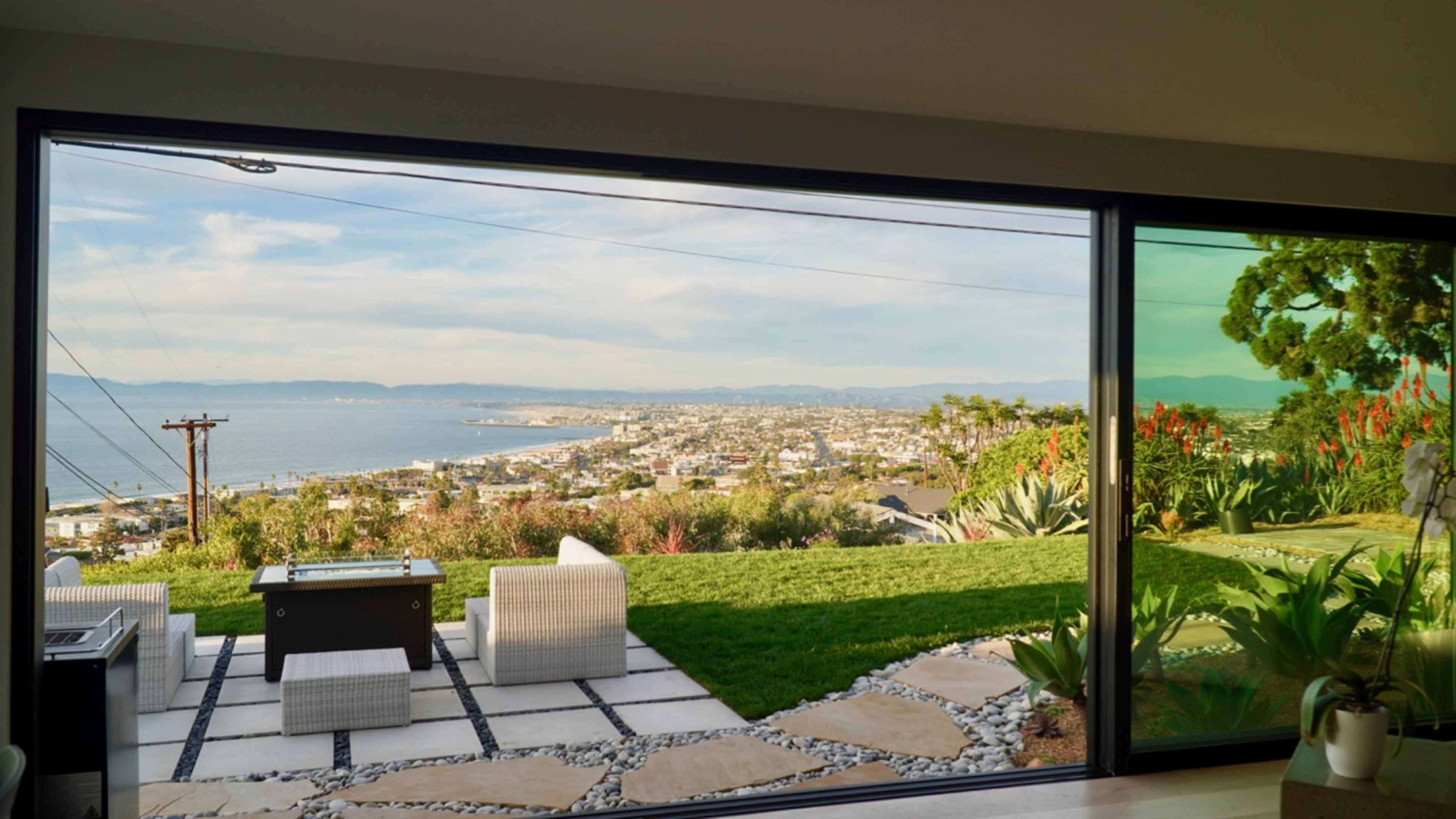A modern living room opens to a coastal view featuring a landscaped garden and the ocean in the distance.
