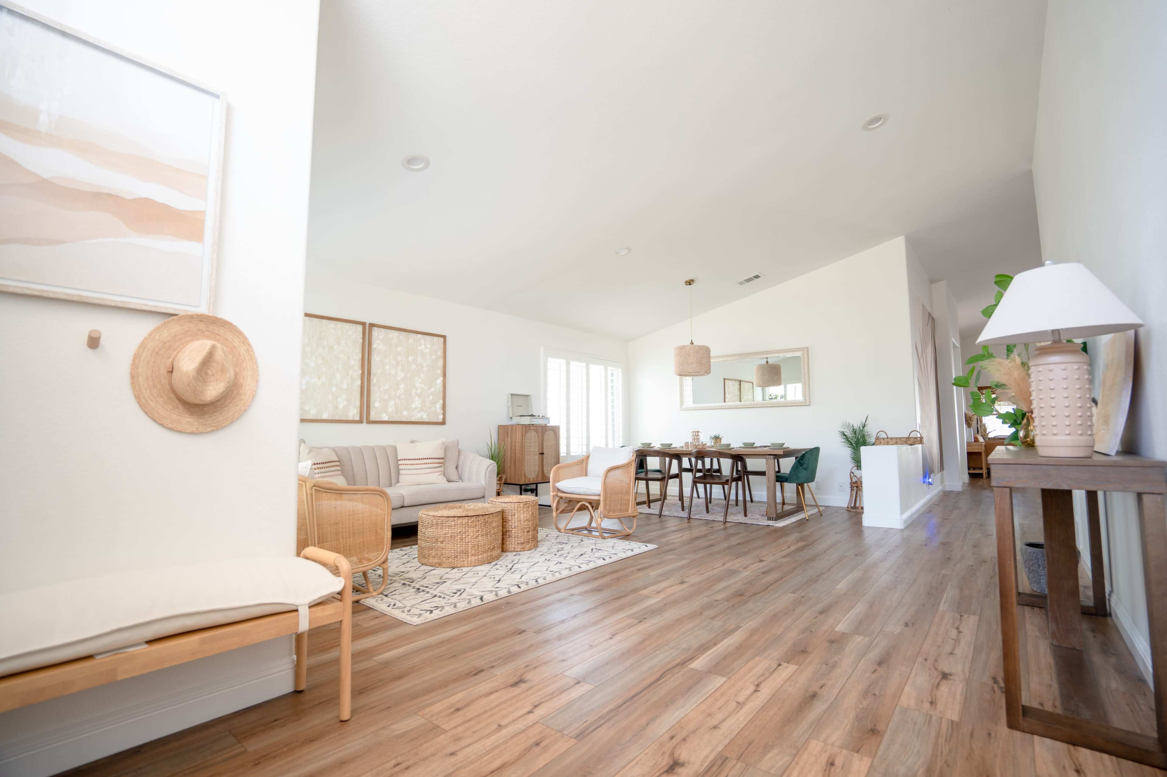 A spacious living area with a sofa, dining table, and natural wood flooring, complemented by light-colored walls and several decorative elements.