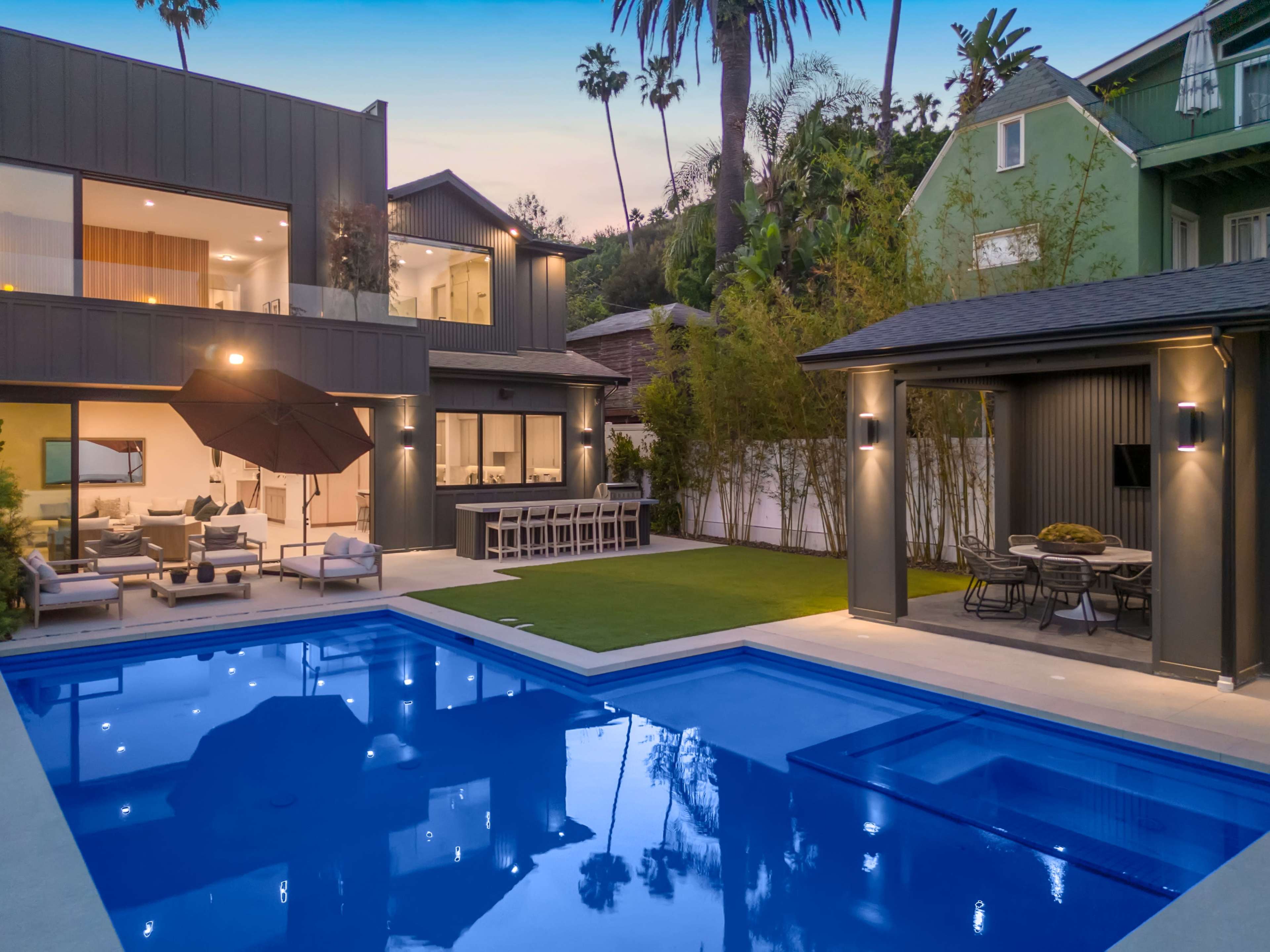 A modern house with a swimming pool is surrounded by palm trees and features outdoor seating areas and a patio.