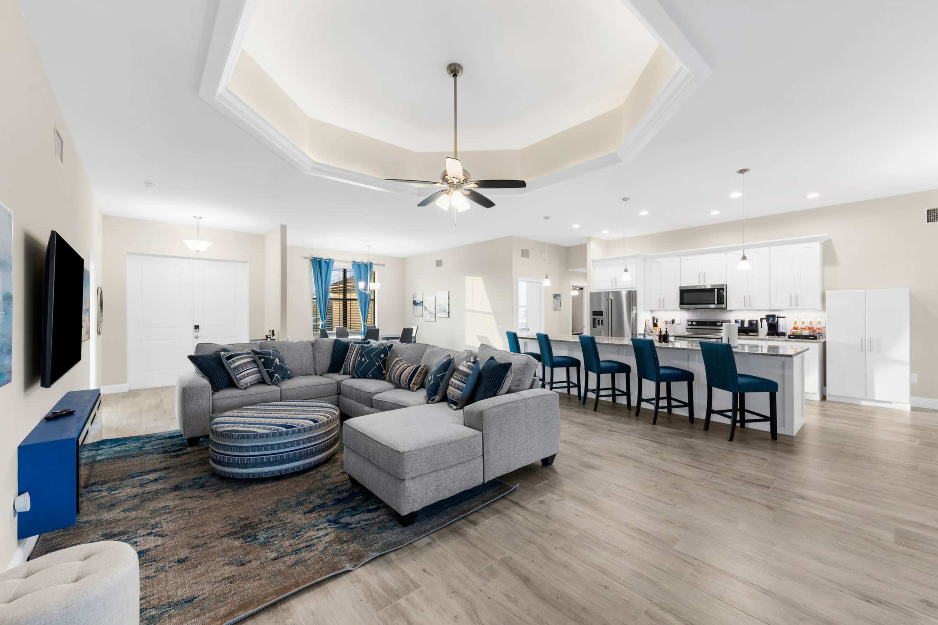 A spacious, modern living area featuring a sectional sofa, accent chairs, and a kitchen bar with high stools.