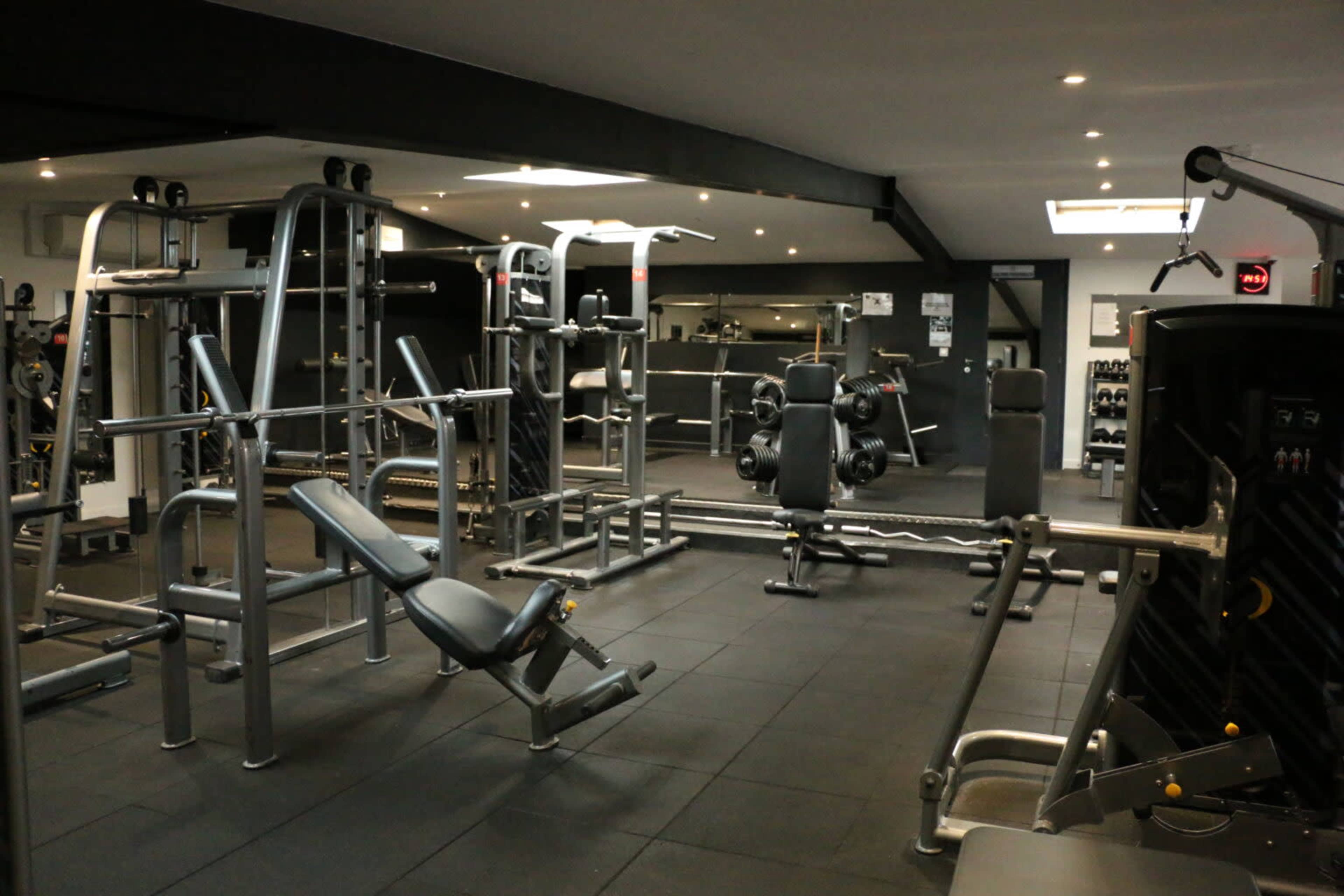 A well-equipped gym featuring various weightlifting machines, benches, and free weights arranged in an open space.