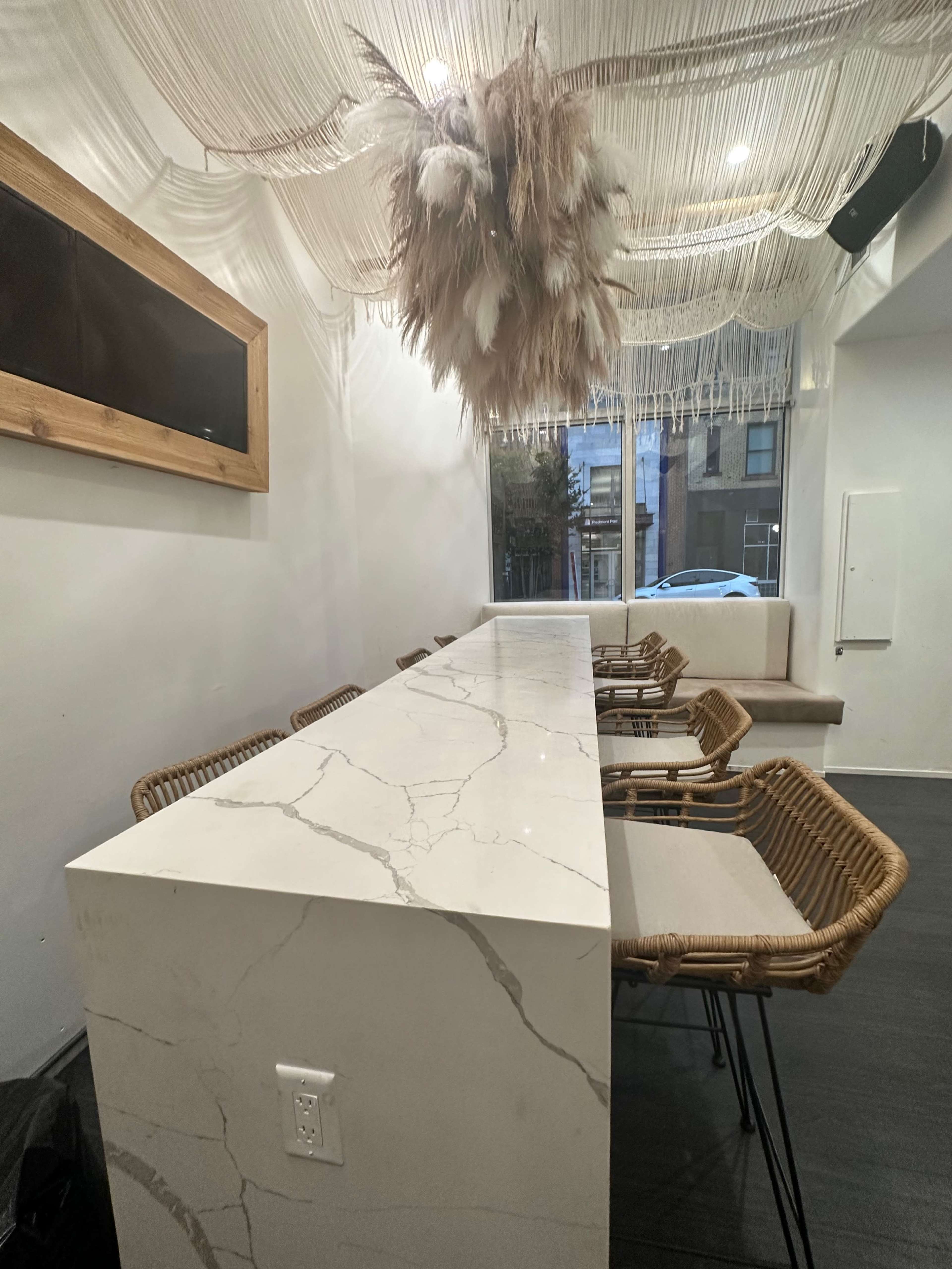 A modern interior with a long marble countertop, wicker chairs, and a decorative hanging installation made of dried plants.