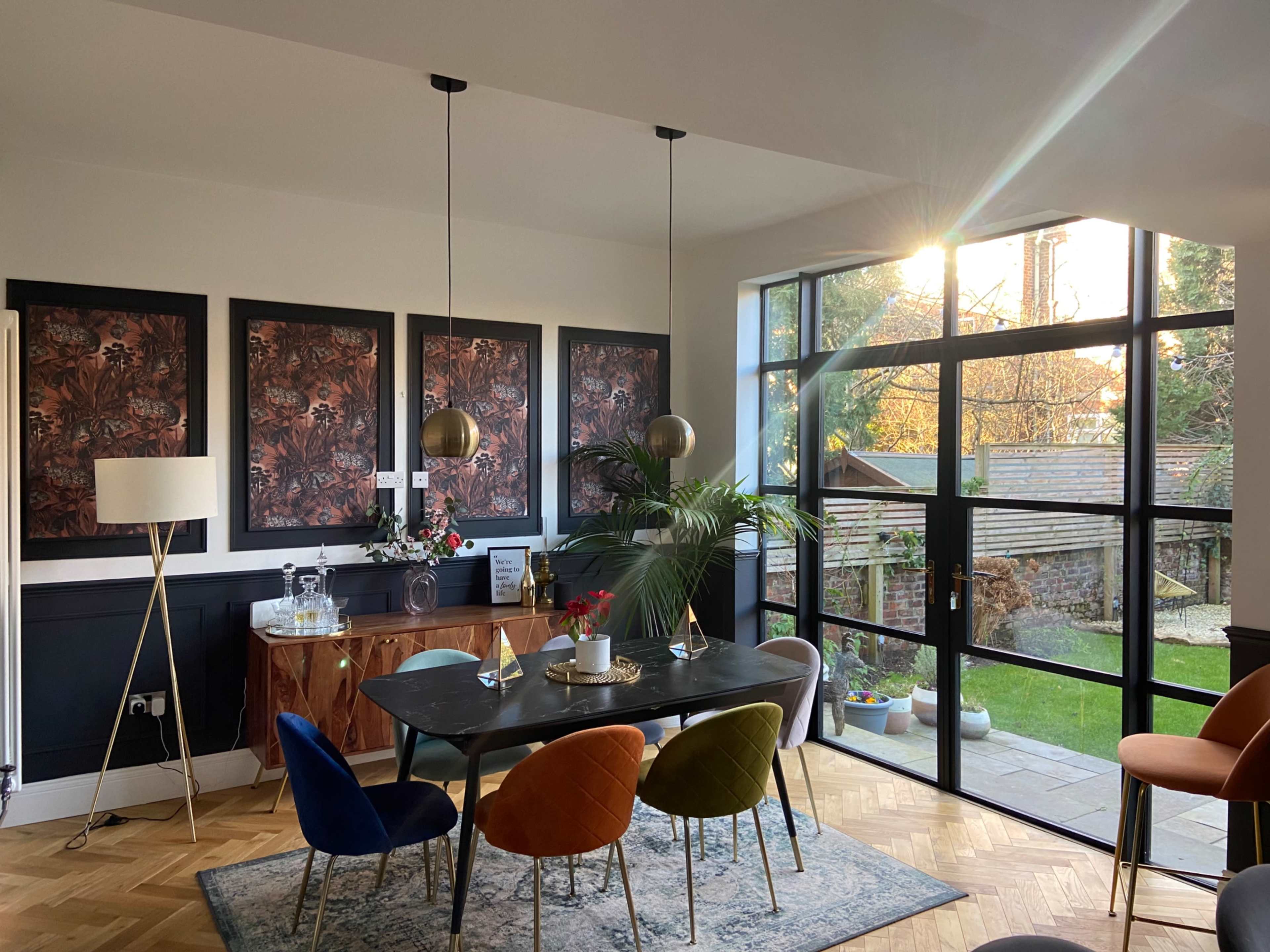 A modern dining area features a large table surrounded by colorful chairs, with floor-to-ceiling windows allowing natural light to illuminate the space.