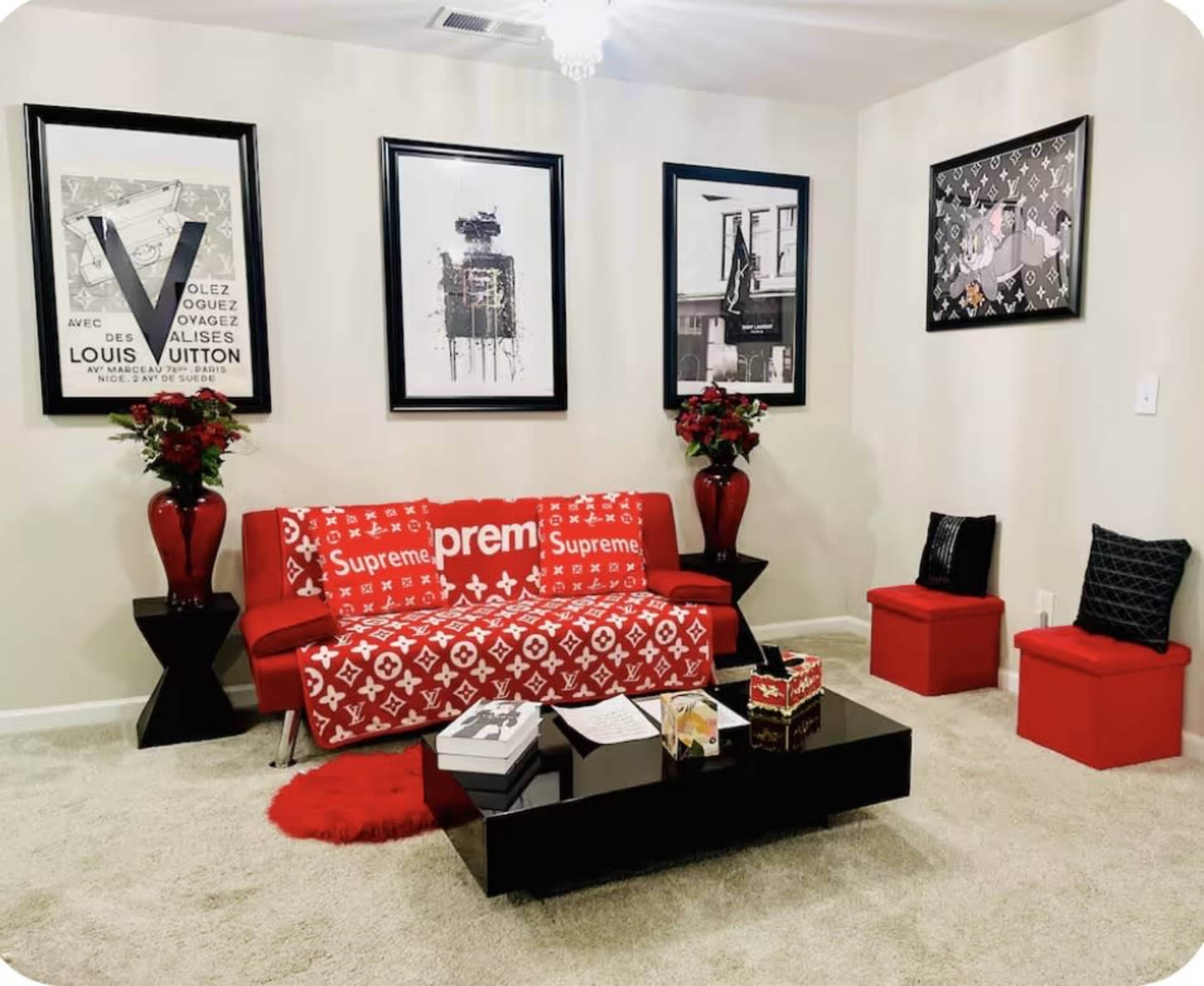 The image depicts a modern living room with a red and white couch, black coffee table, and framed art pieces on the walls, accented by red floral arrangements and decorative pillows.