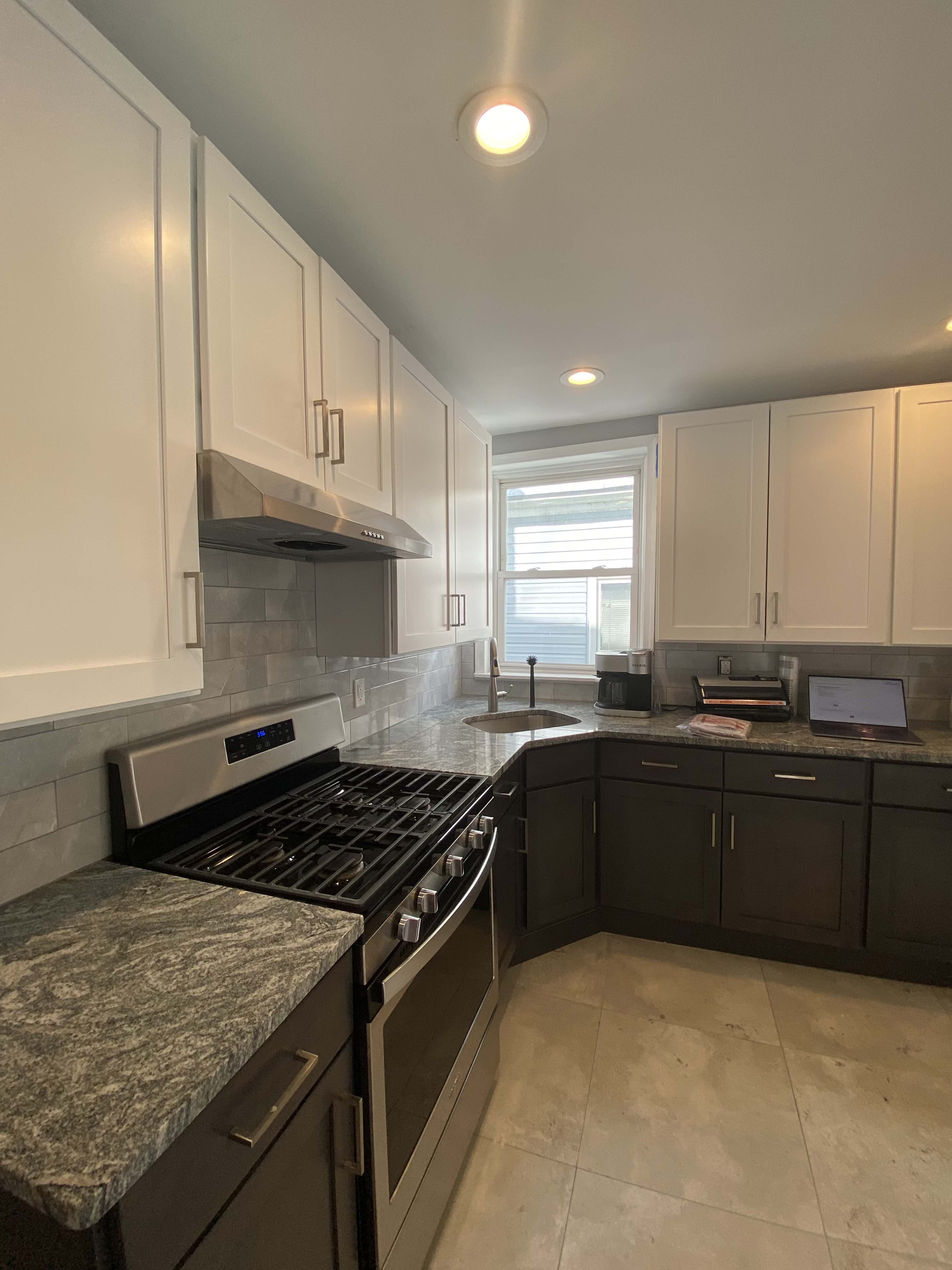 A modern kitchen features a combination of white and dark cabinetry, a stainless steel gas stove, and a window providing natural light.