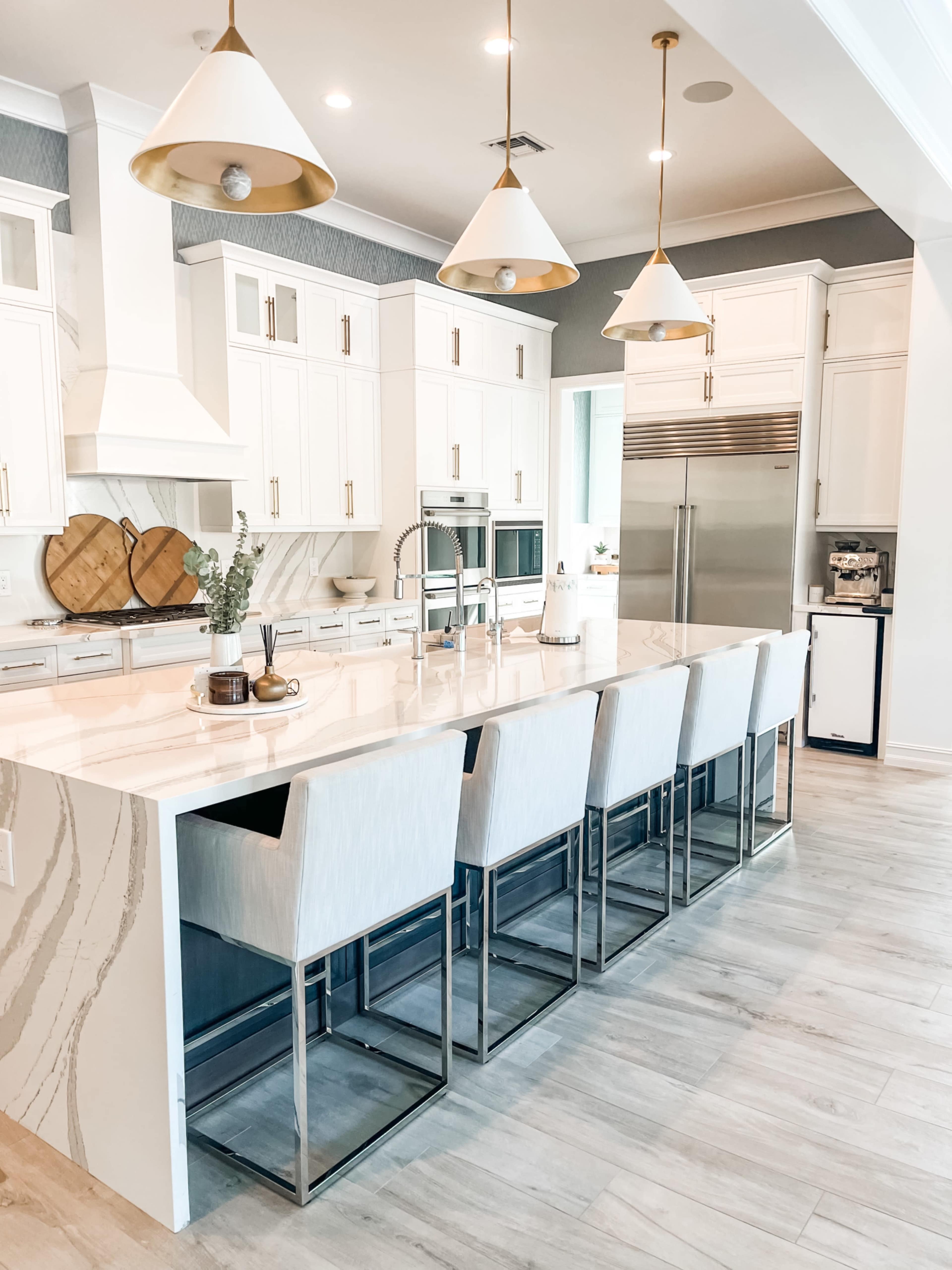 A modern kitchen features a large island with bar seating, white cabinetry, and pendant lighting.