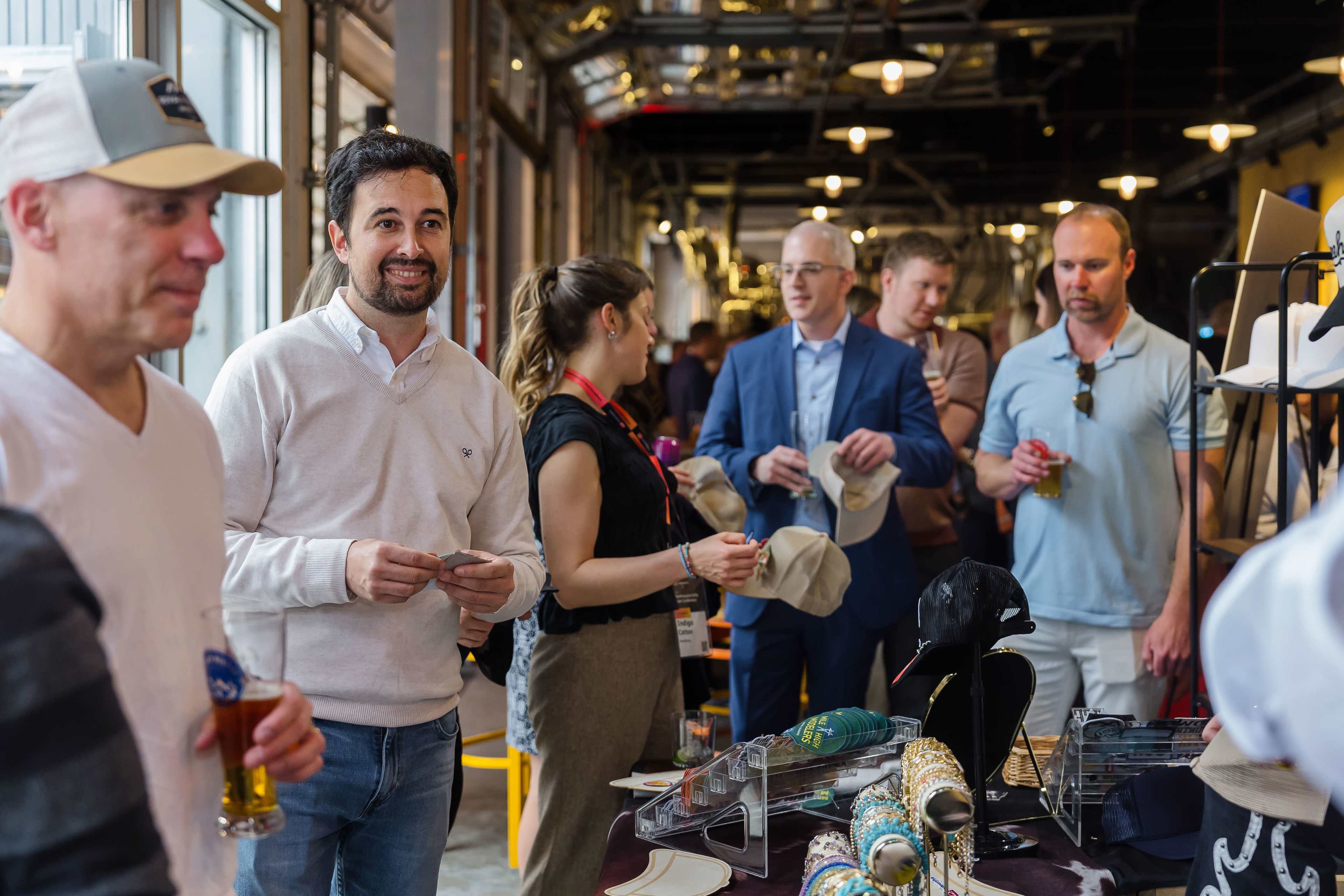 People are gathered at a marketplace or event, looking at various hats and engaging in conversation.