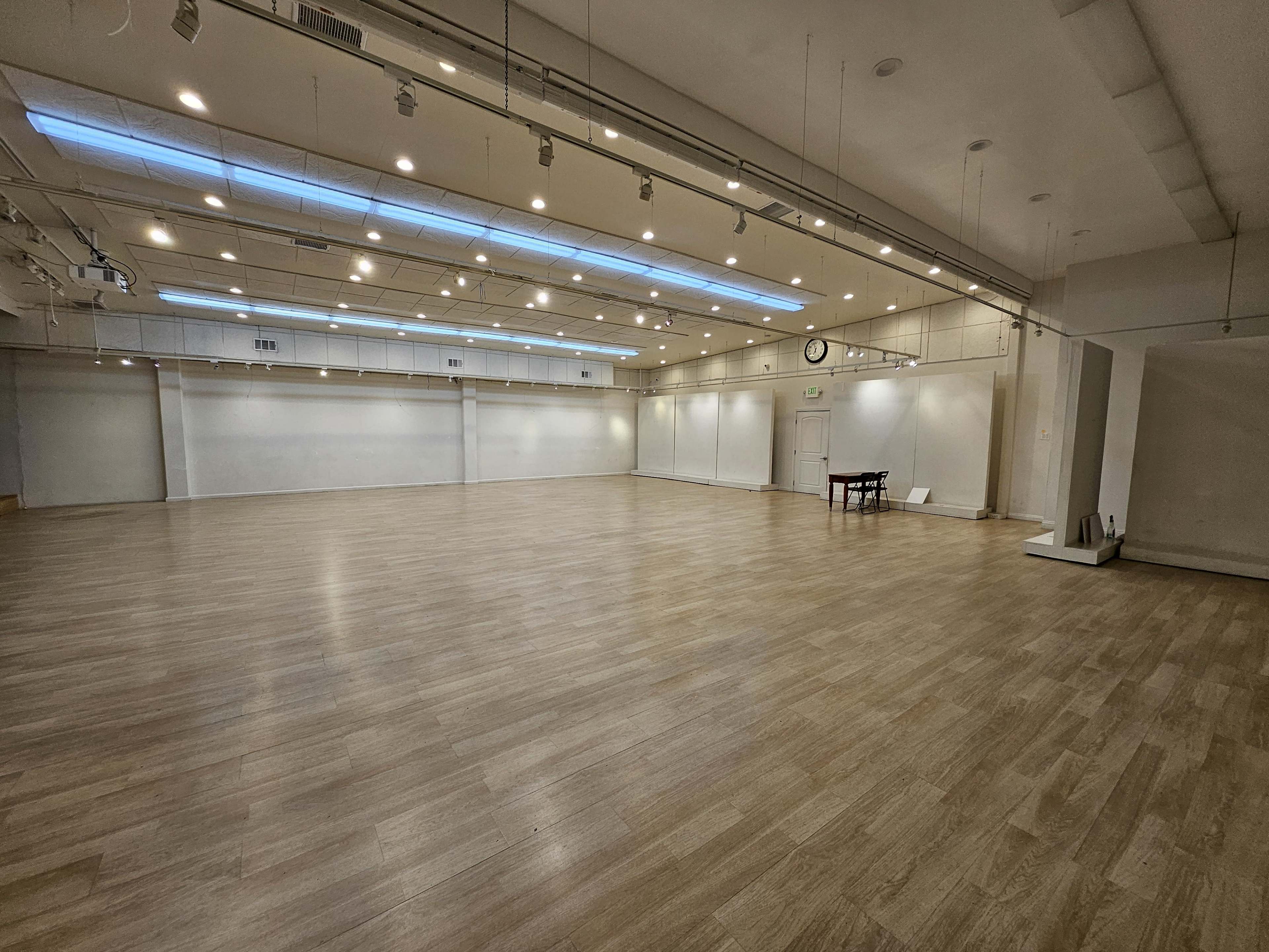 An empty, well-lit room with wooden flooring and a single table against one wall.
