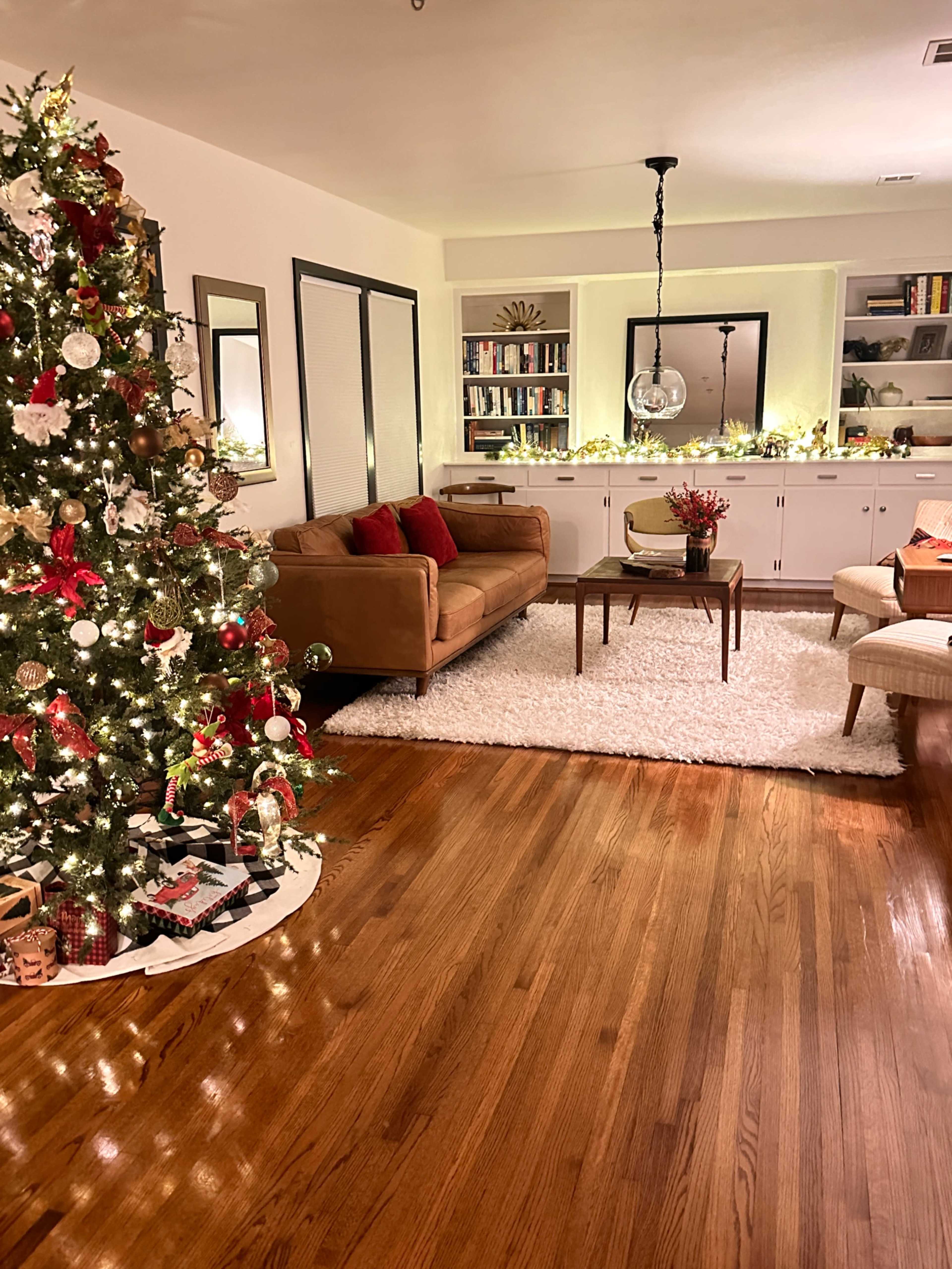 The living room features a decorated Christmas tree, a brown sofa with red cushions, and a coffee table on a plush white rug.