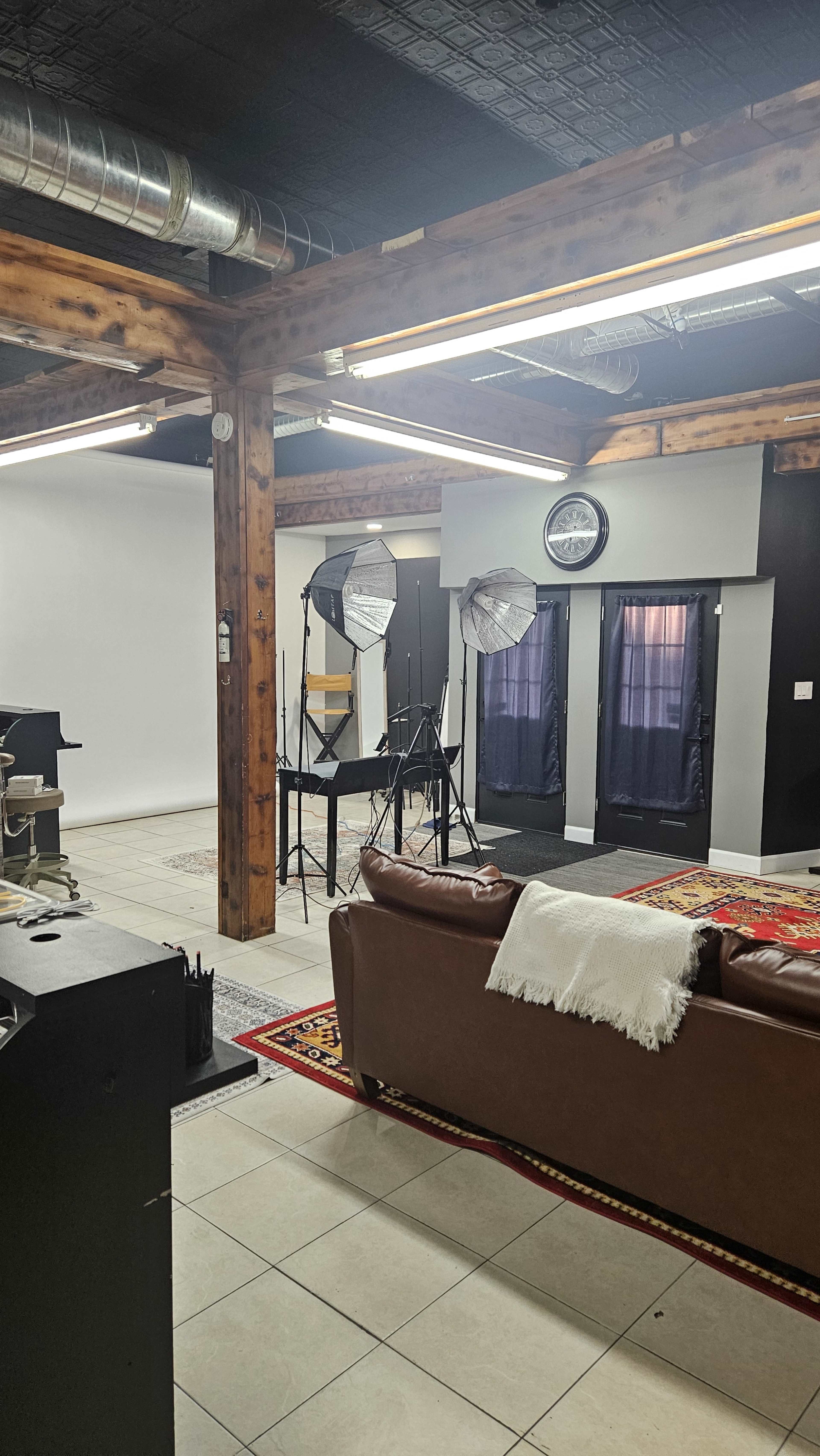 The image shows a spacious studio with a brown sofa, photography equipment including light stands, and a backdrop area in a well-lit setting.