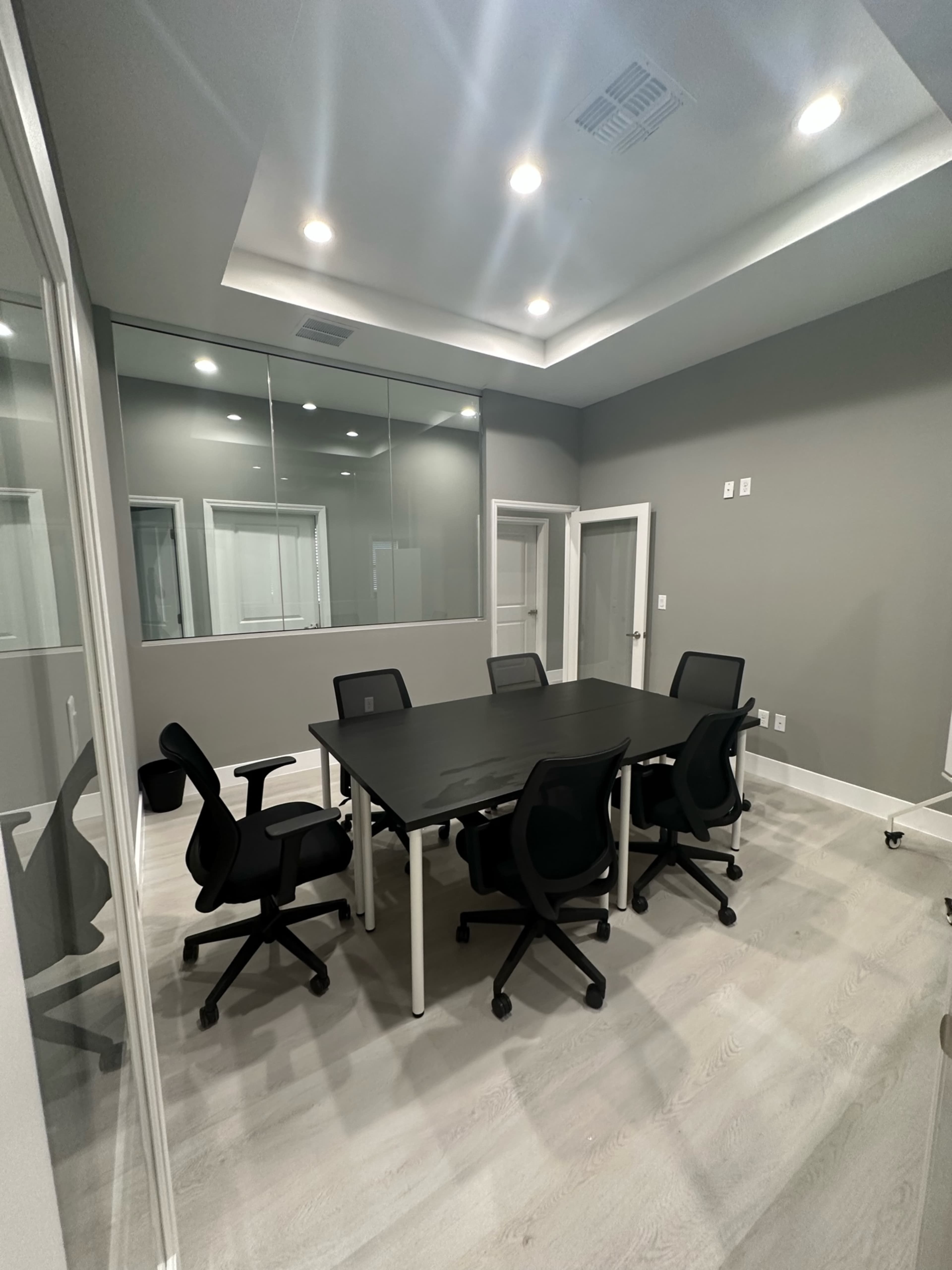 The image shows a modern conference room featuring a large black table surrounded by six black chairs, with glass walls and ample lighting.