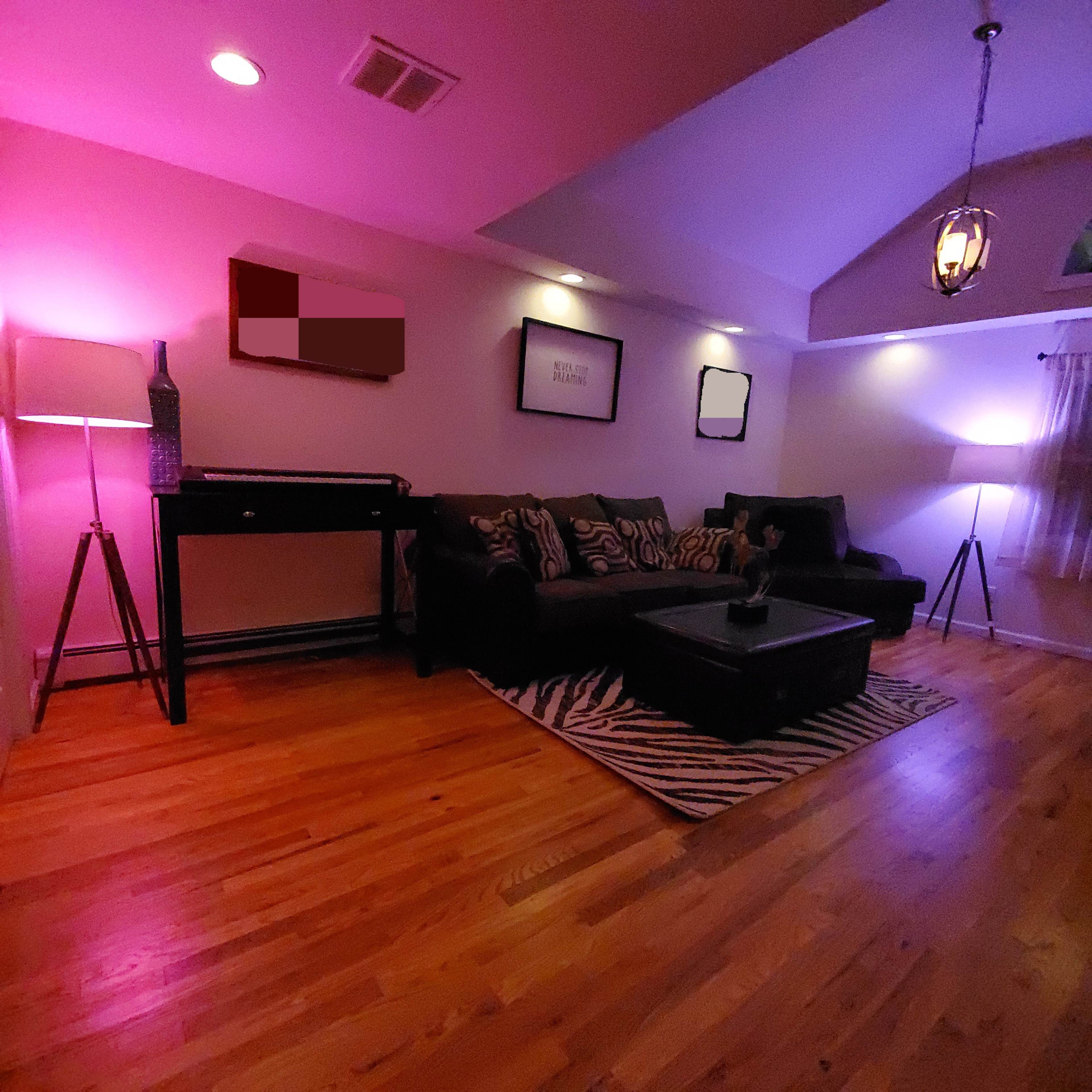 A living room features a dark couch and coffee table on a striped rug, illuminated by ambient purple lighting and lamps.