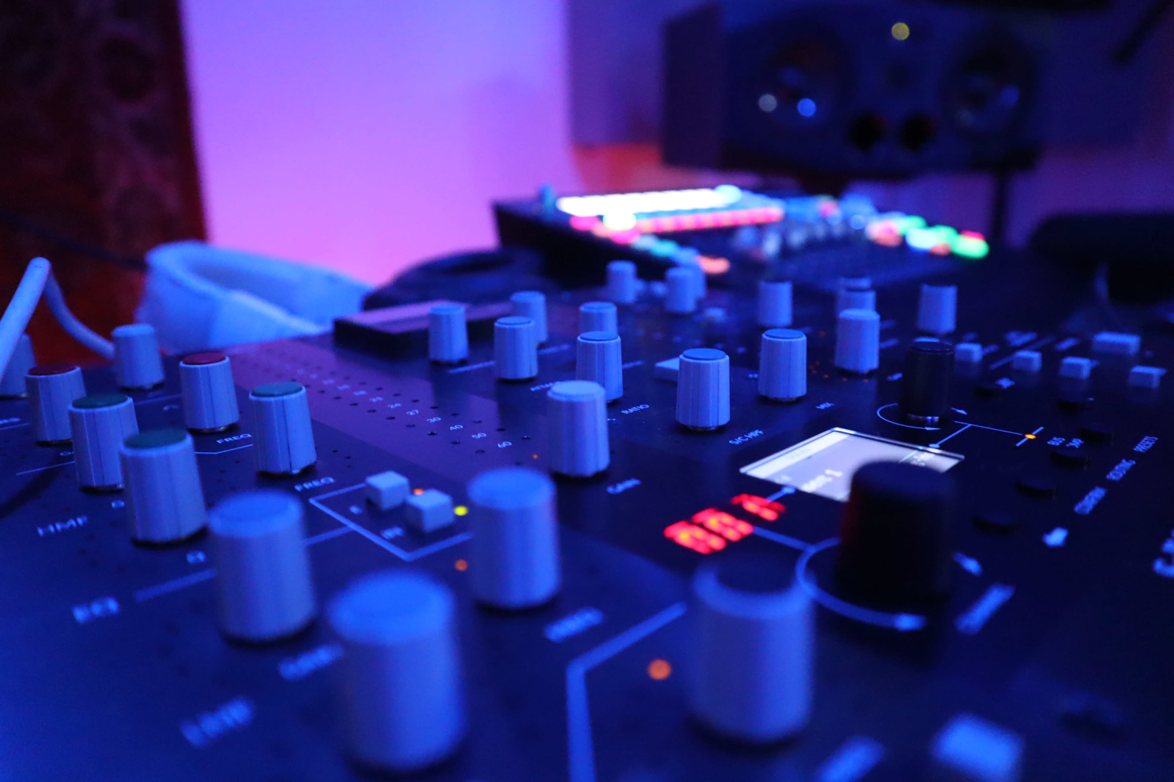 A close-up view of a music production mixer with various knobs and buttons, illuminated by blue and colorful lights in the background.