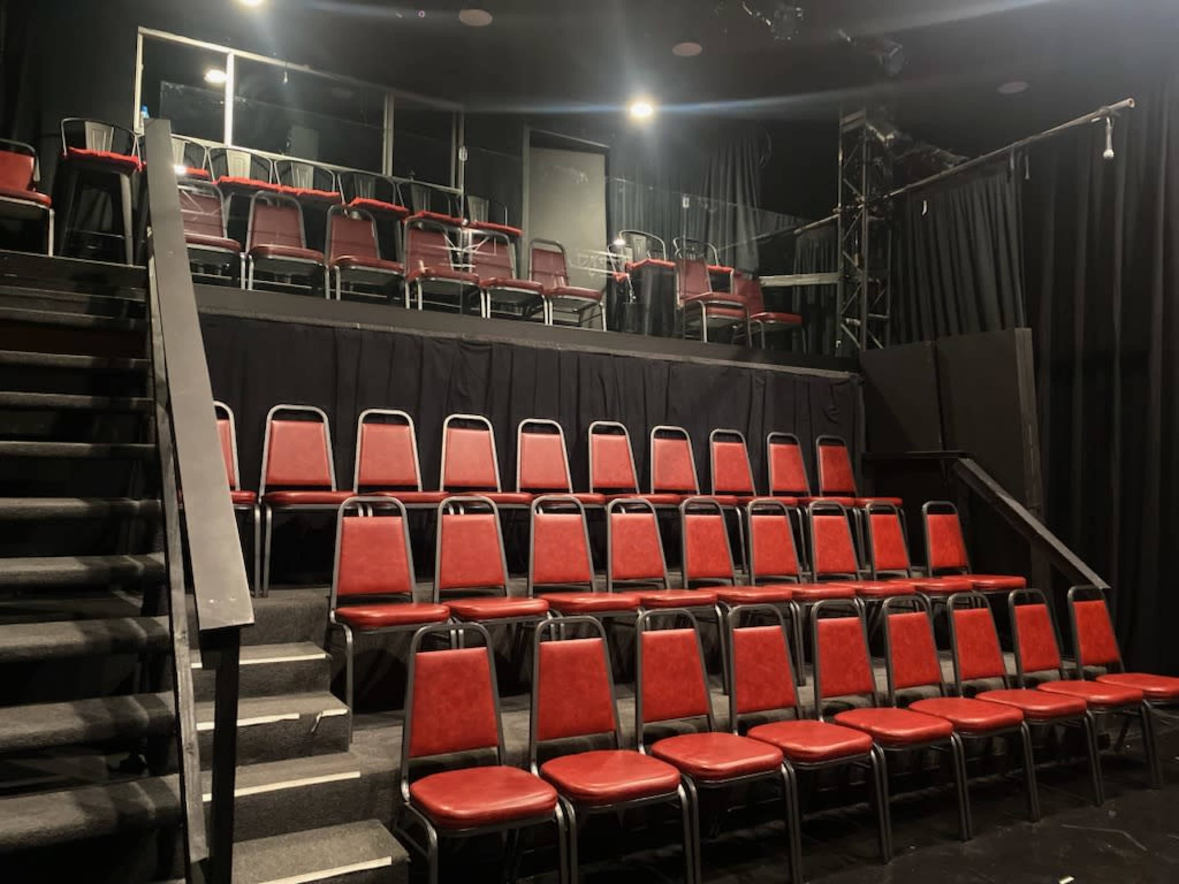 A theater stage with rows of red chairs and a staircase leading up to the seating area.