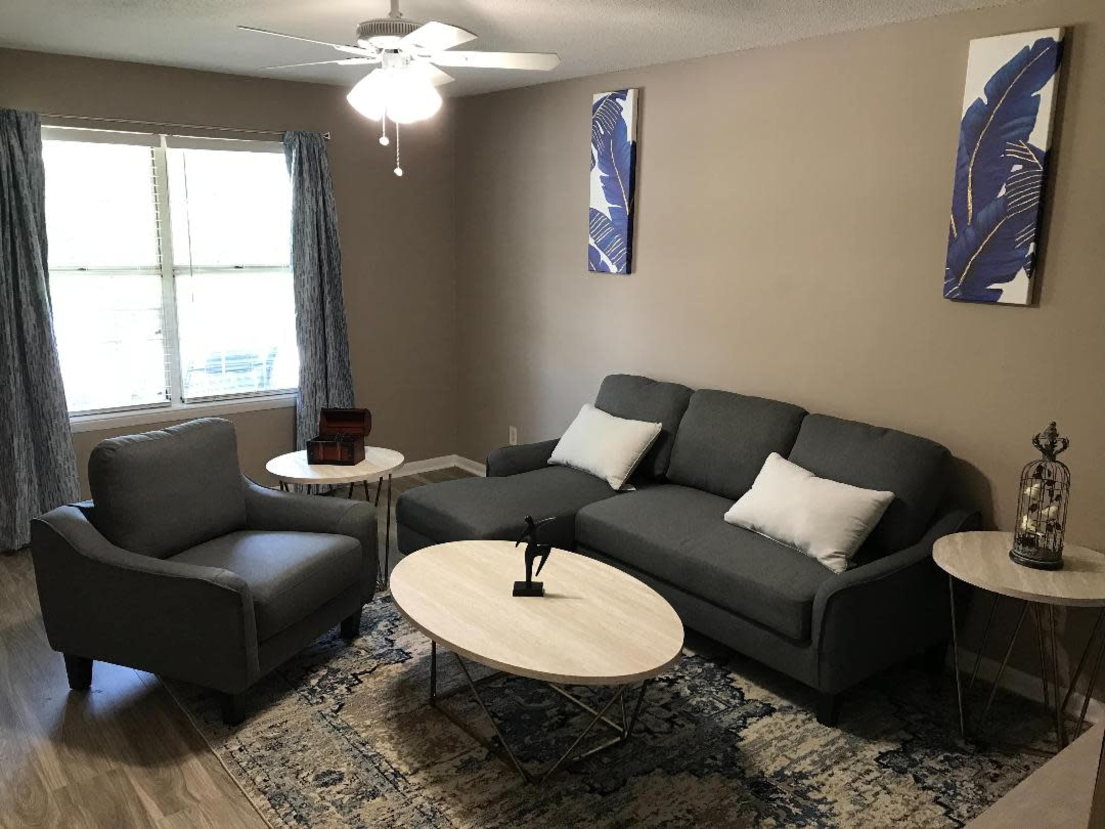 A living room with a gray sofa, a matching armchair, a round table, and decorative artwork on the walls.