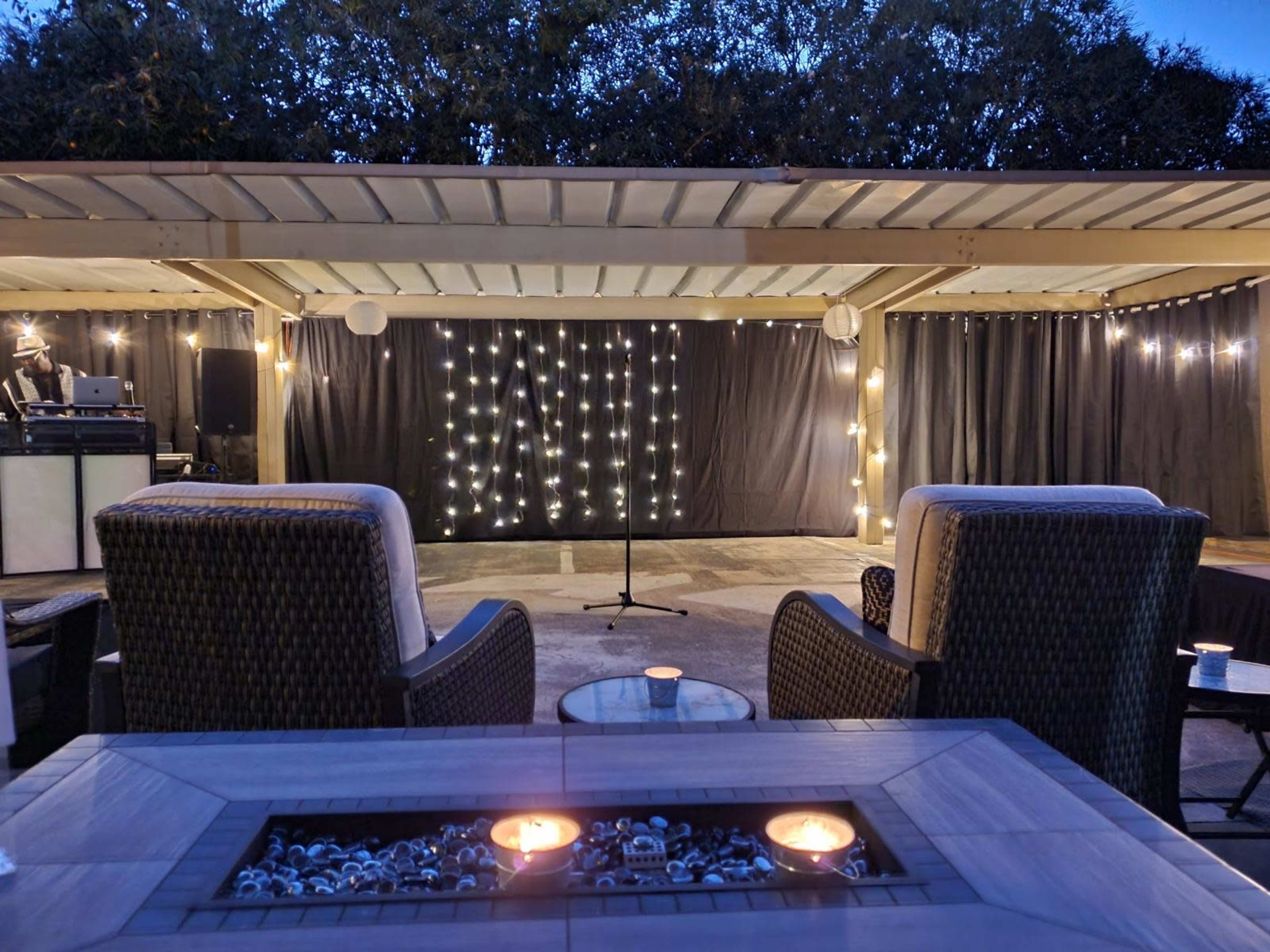 A cozy outdoor seating area features two chairs facing a stage adorned with string lights under a covered patio.