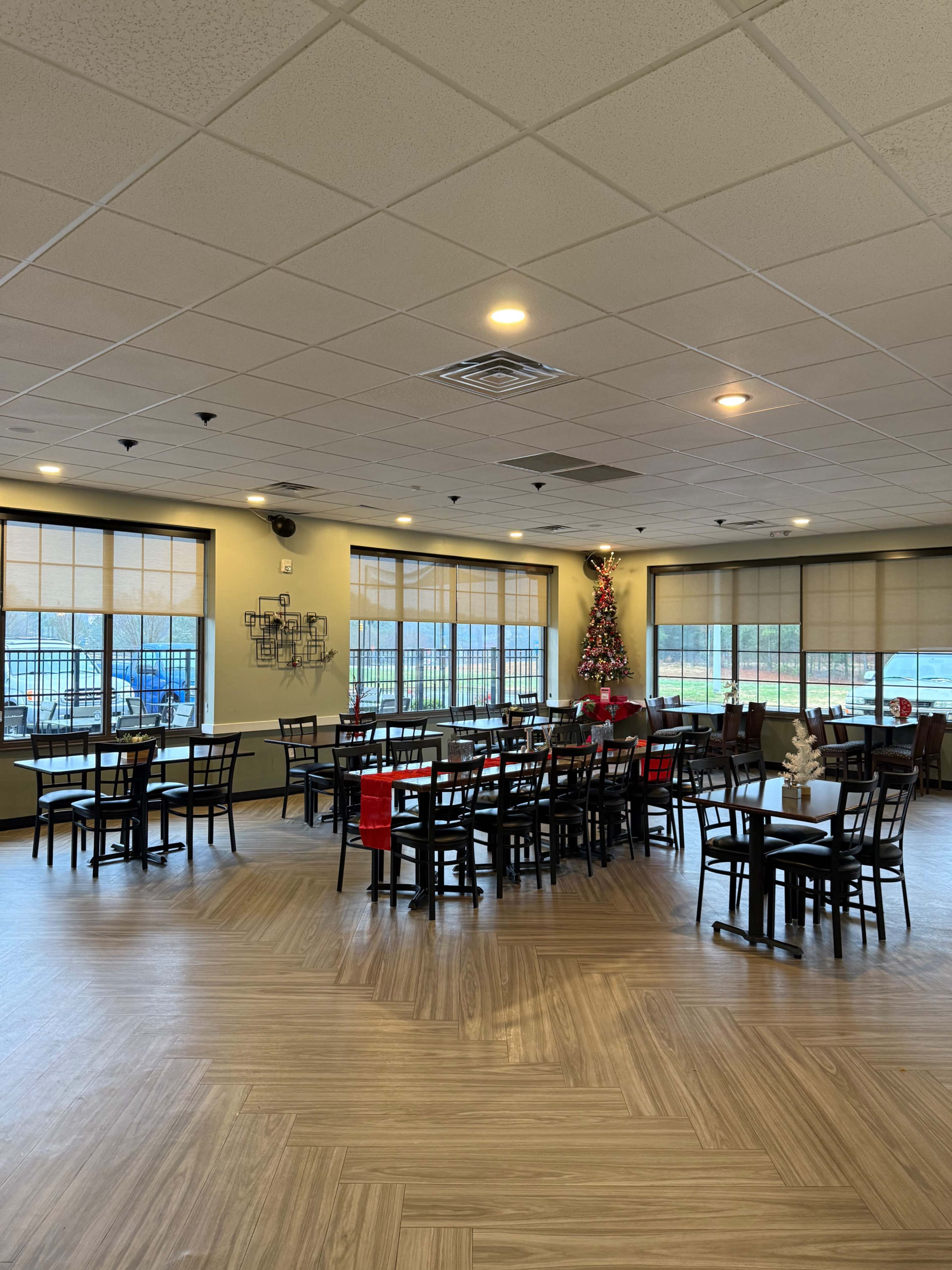The image shows a spacious dining area with multiple tables and chairs, large windows, and a Christmas tree in one corner.