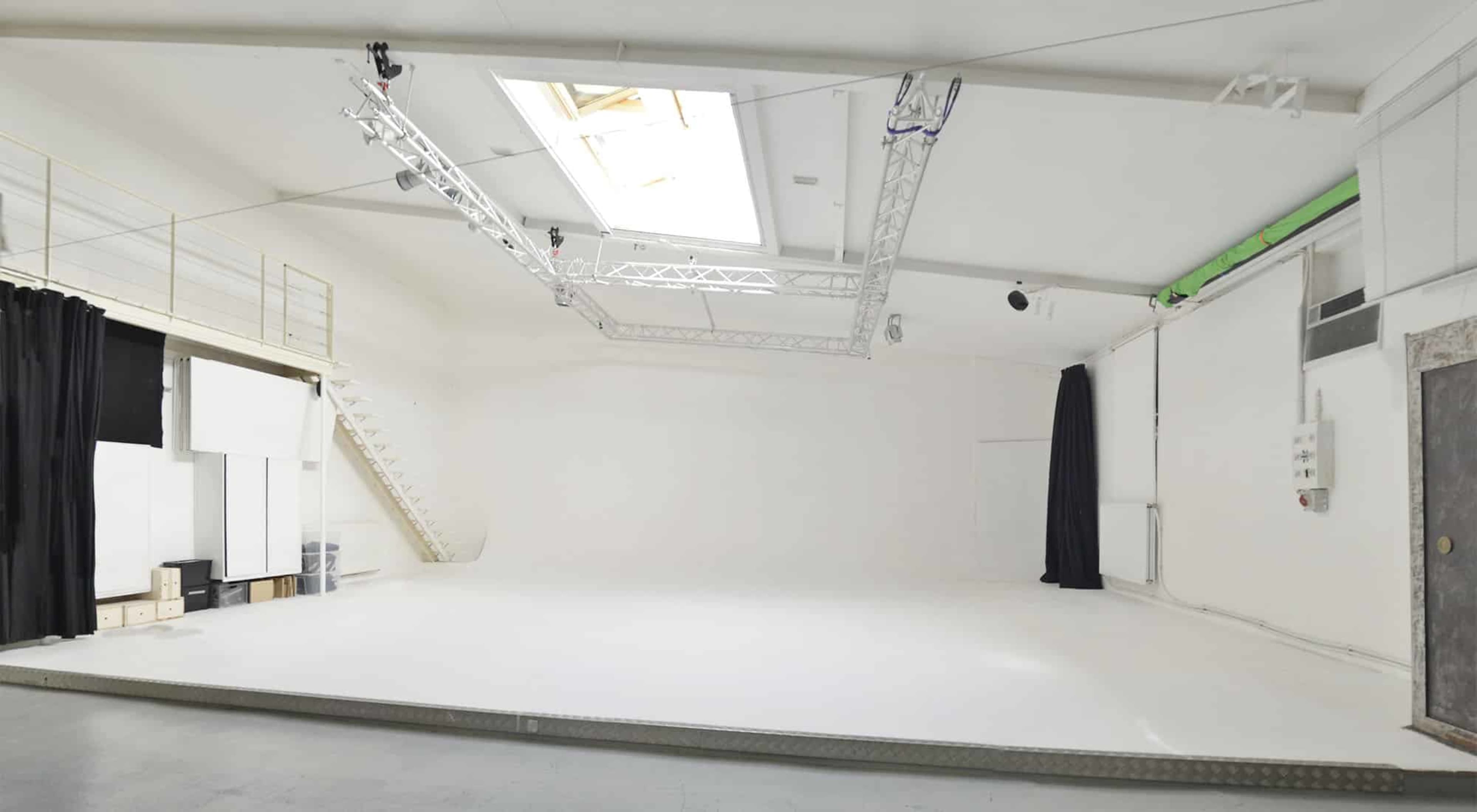 The image shows a spacious, empty studio with white walls, a smooth floor, and a skylight above.