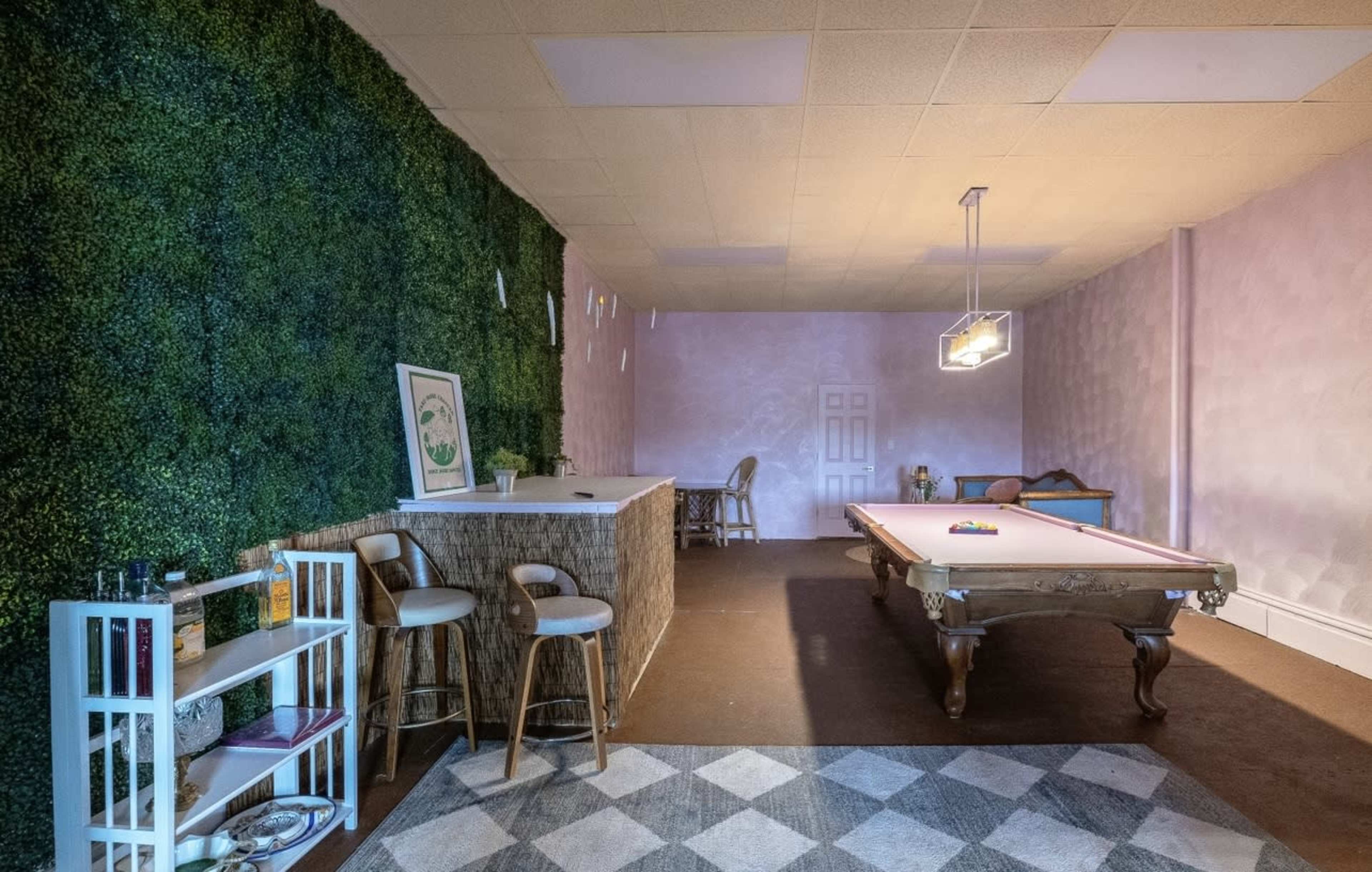 A room with a green wall, a pool table, a bar area with stools, and a patterned carpet.